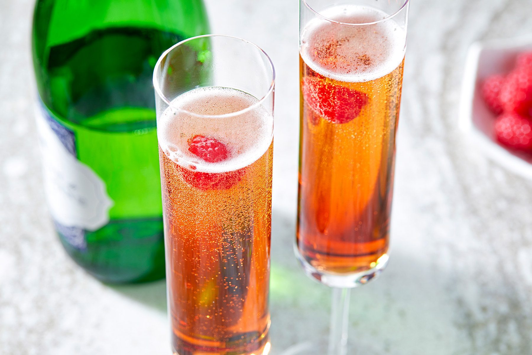 High angle view shot of kir Royale; Champagne bottle; raspberries bowl; marble background;