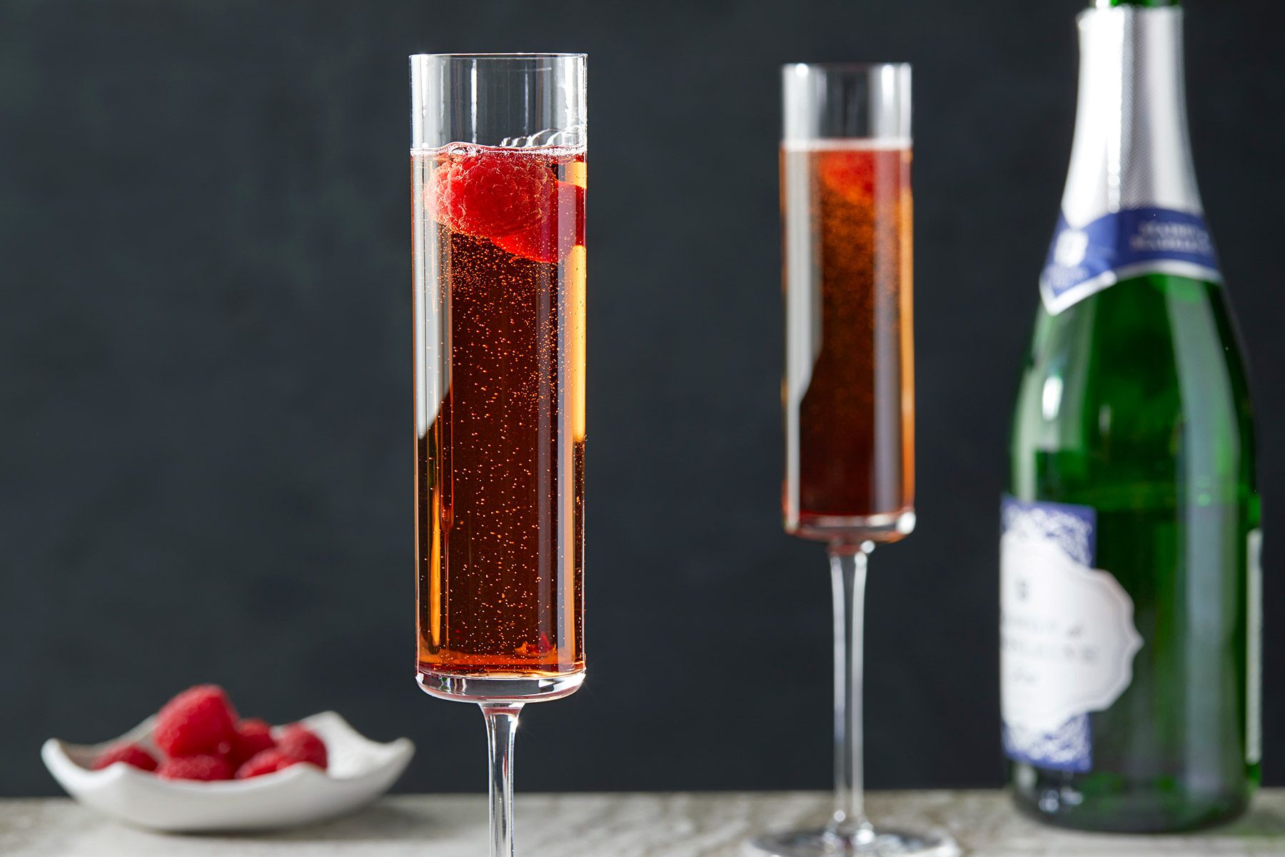 Table view shot of kir Royale; Champagne bottle; raspberries bowl; marble background;