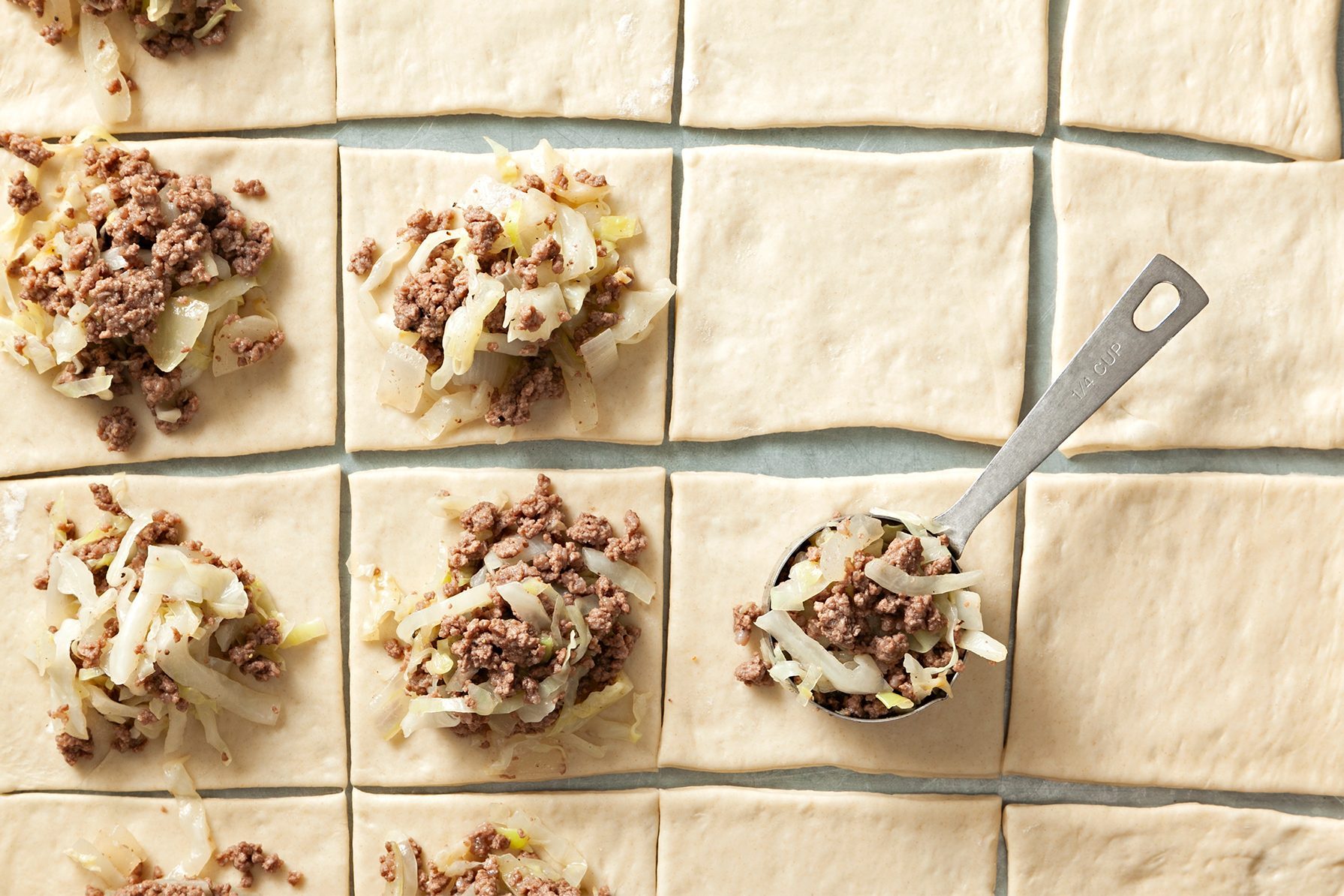 Square pieces of dough arranged in a grid, each topped with a mixture of cooked minced meat and shredded cabbage. 