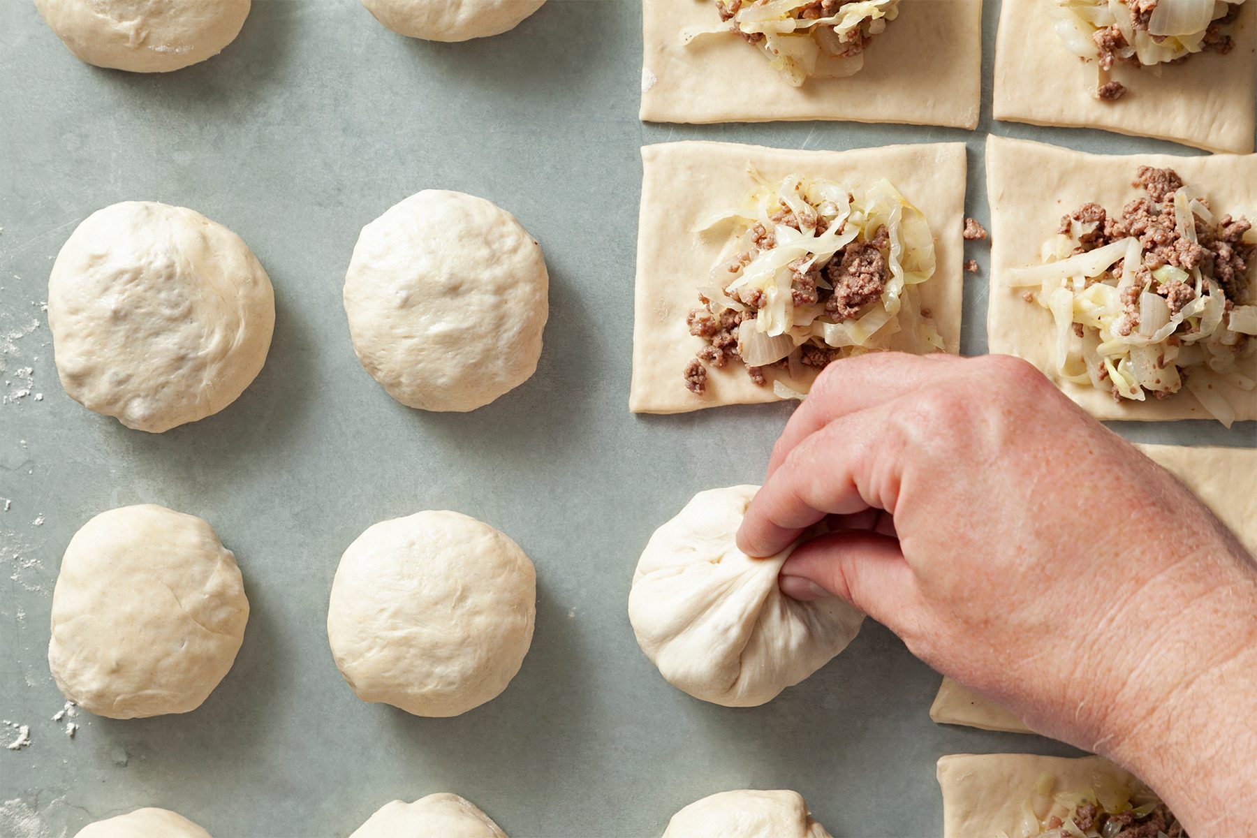 A hand is pinching a dough ball filled with a mixture of meat and chopped vegetables. 