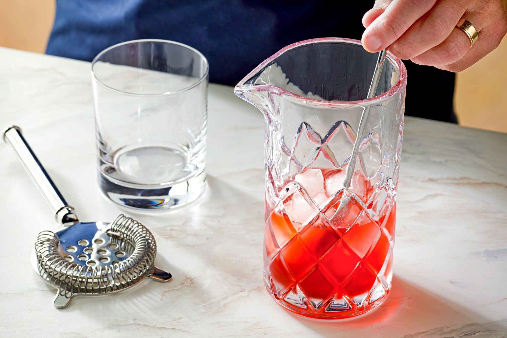 mixing campari, gin and sweet vermouth in a mixing glass with ice; marble surface;