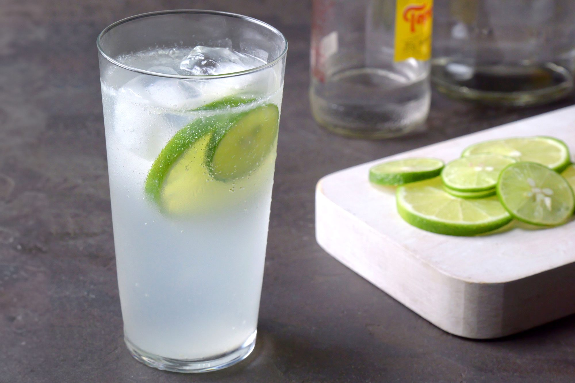 3/4 angle view shot of Ranch Water; served in glass; garnished with lime slices; wooden chopping board; black texture background;