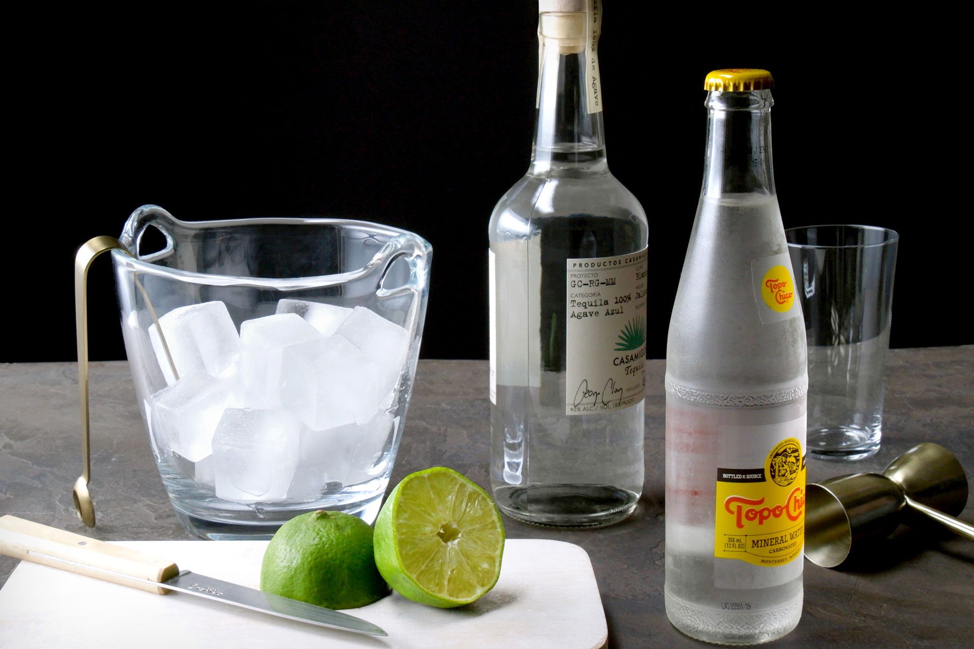 Table view shot of all ingredients for ranch water; knife; chopping board; black texture background;