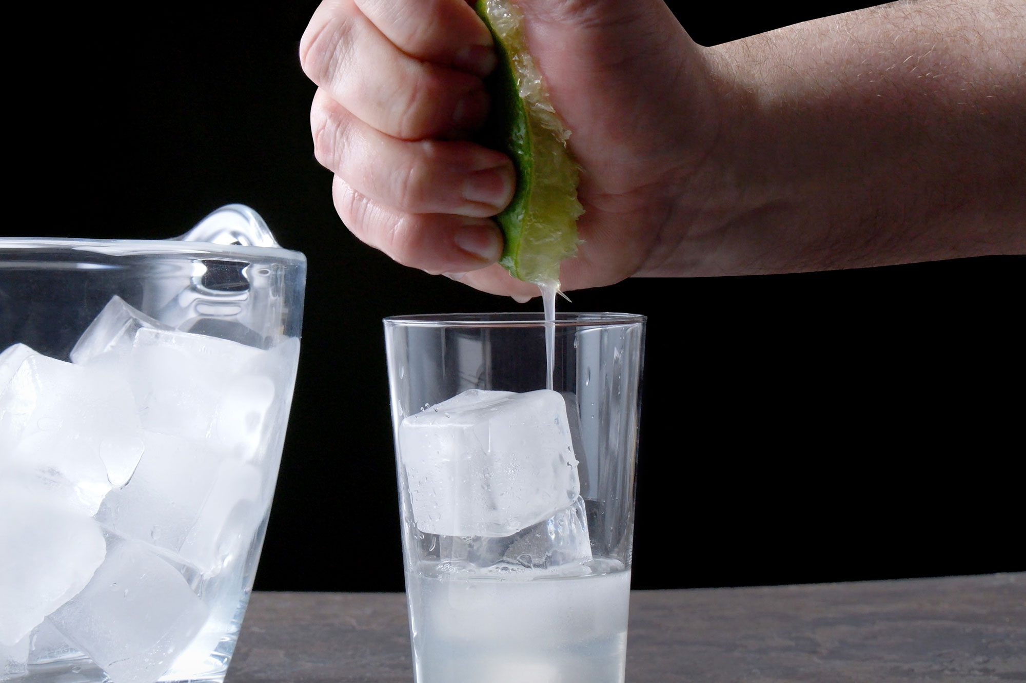 Table view shot of squeeze lime into glass; ice jar; black texture background;