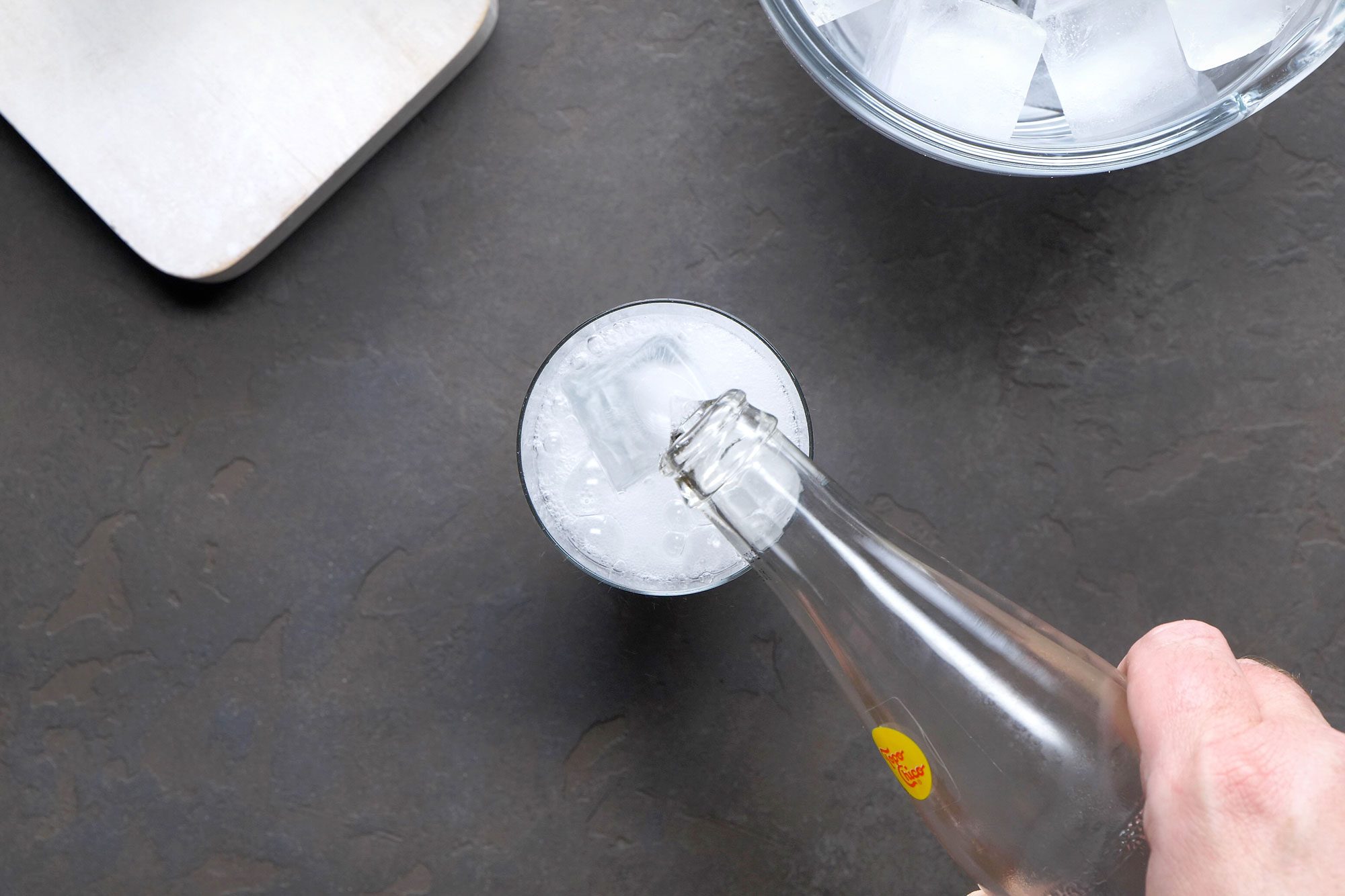 Table view shot of pouring mineral water into a highball glass and stir; ice jar; black texture background;