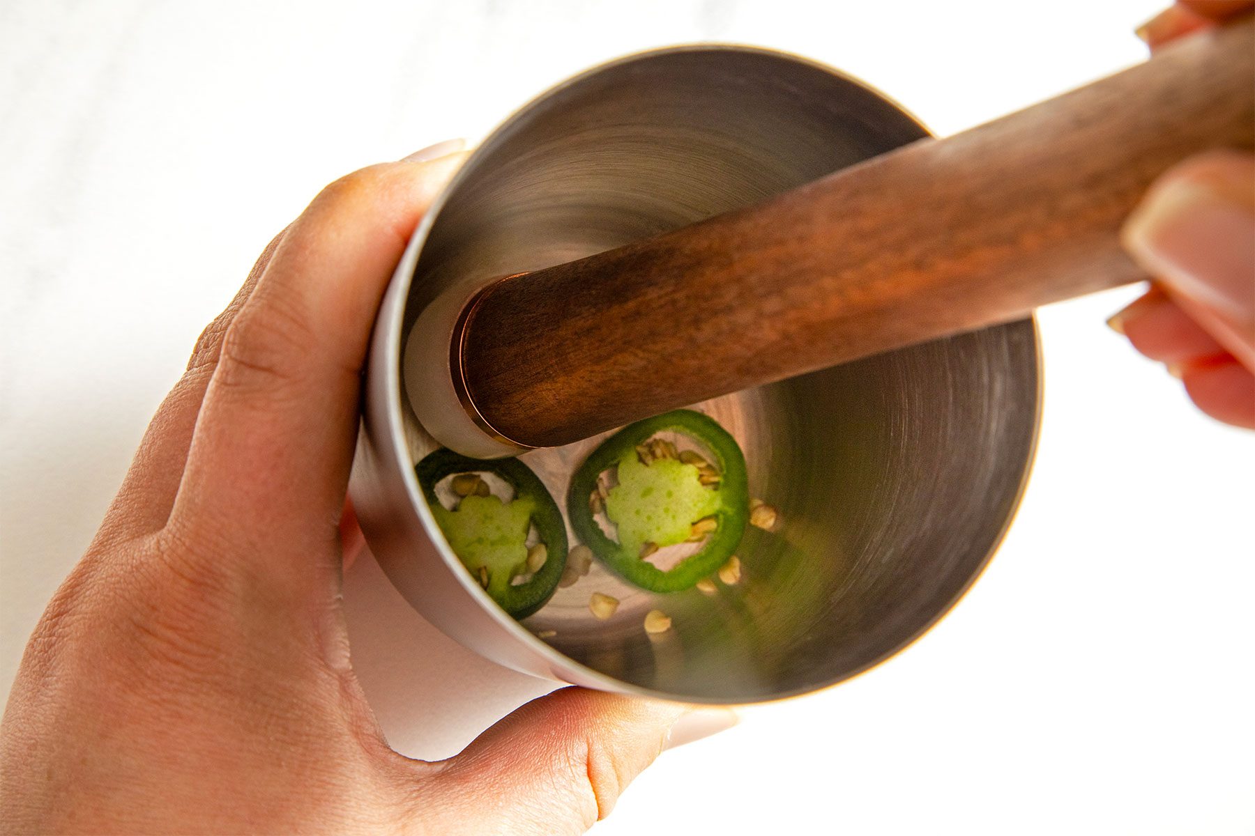 close shot of muddling jalapeno pepper slices in a cocktail shaker