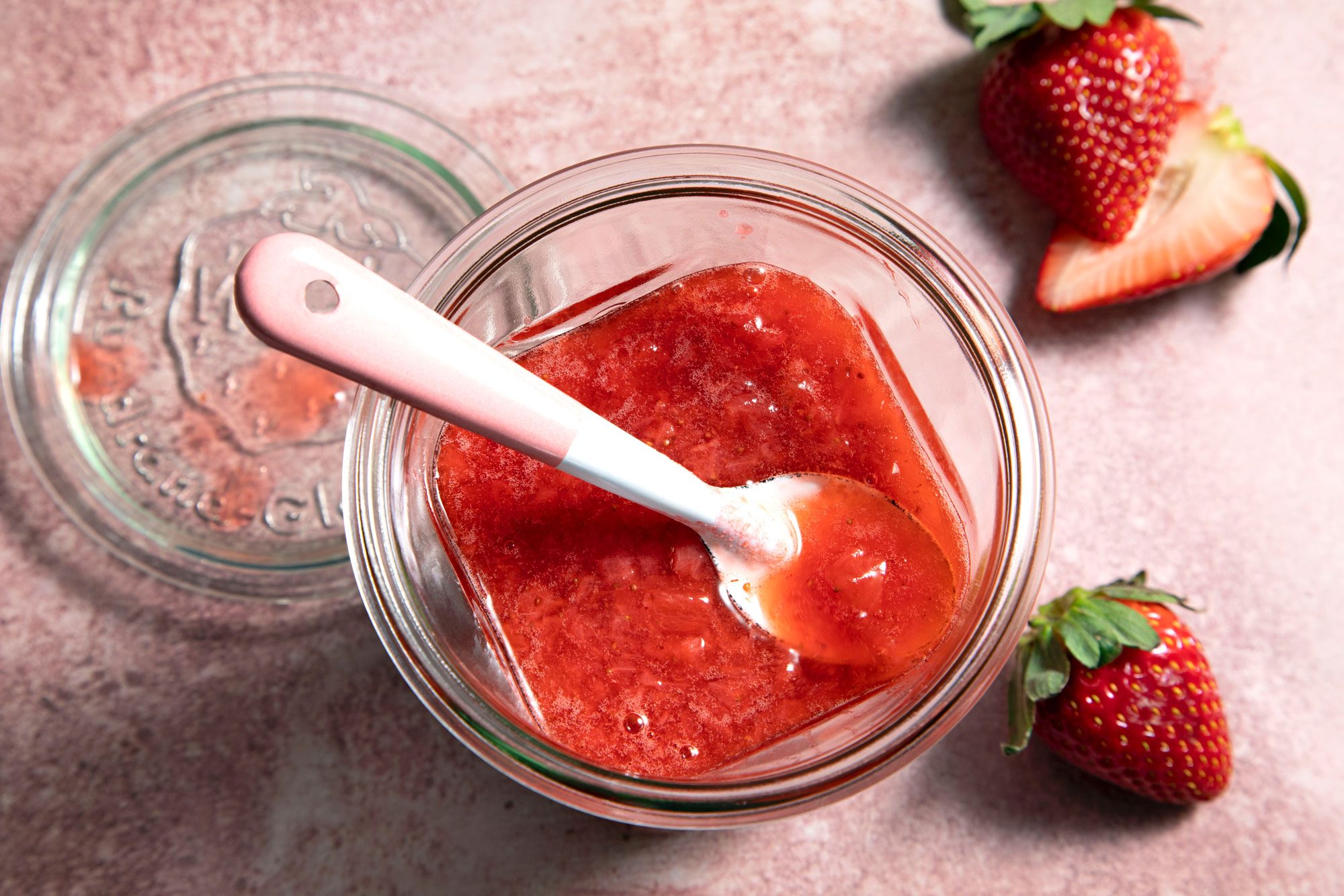 A jar of Strawberry Compote with a spoon and fresh strawberries