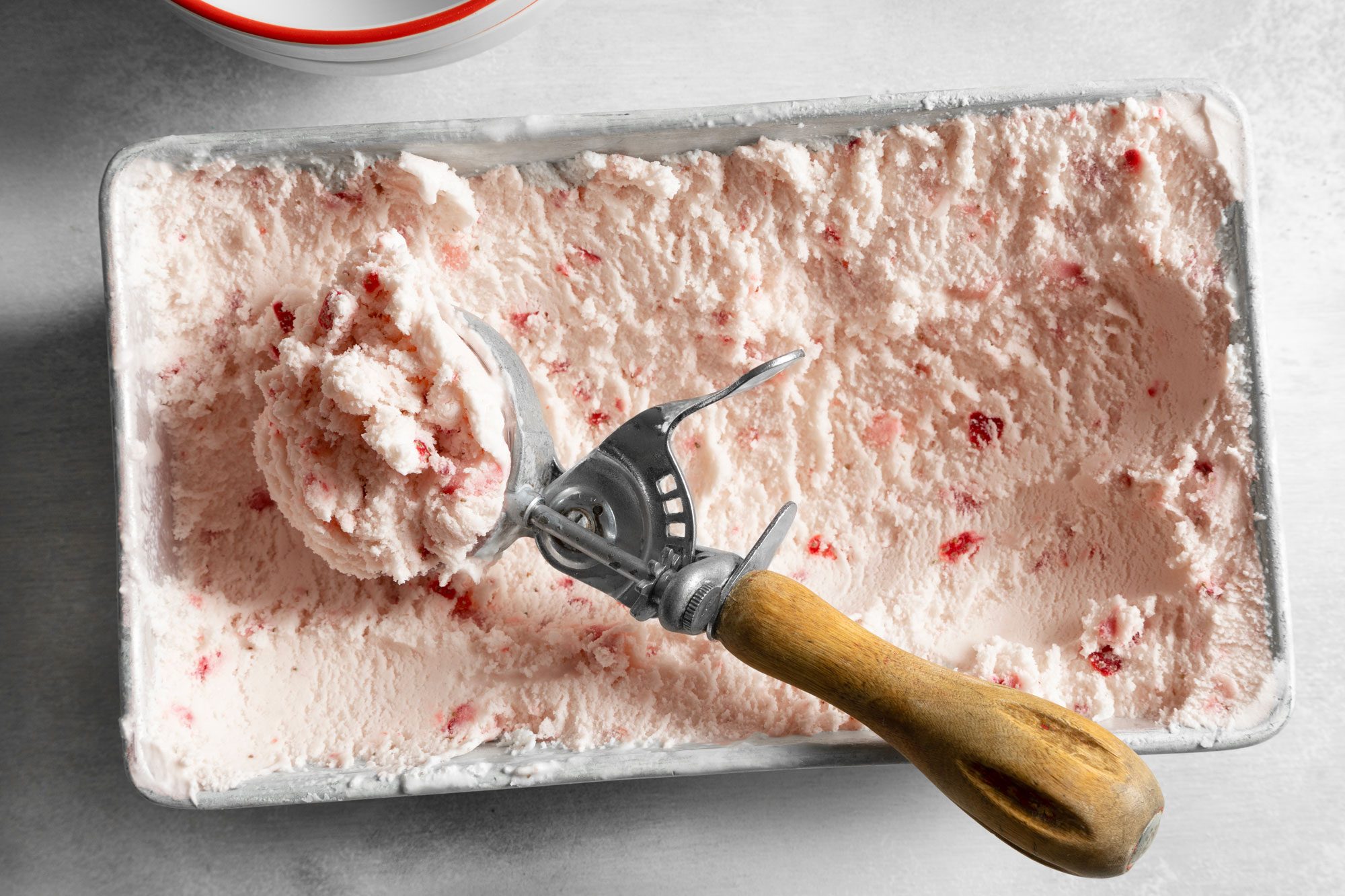 Overhead shot of Strawberry Ice Cream in freezer container, ice cream scoop, white marble background
