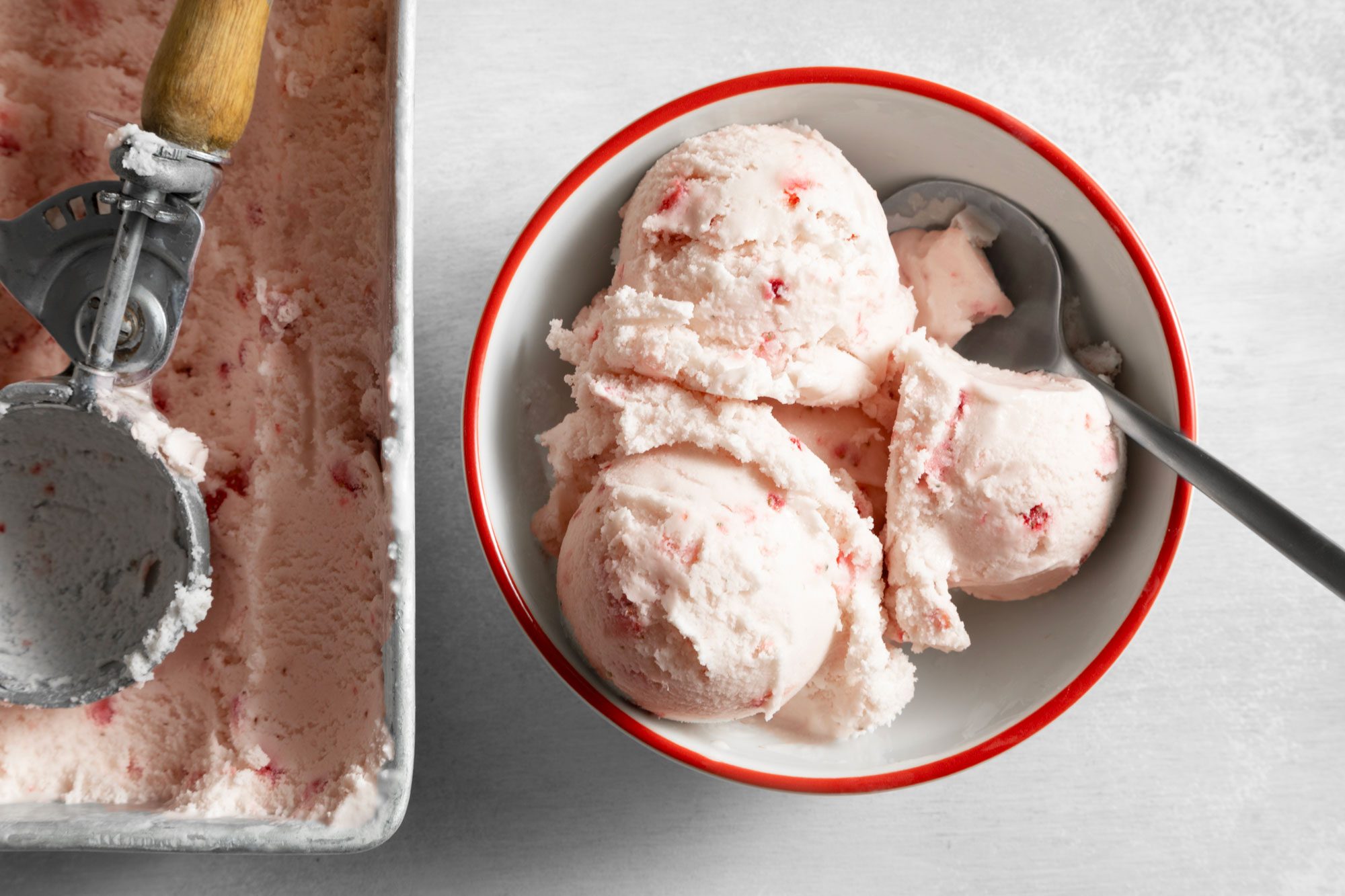Overhead shot of Easy Strawberry Ice Cream served in bowl with spoon; ice cream container; scoop; white marble background;