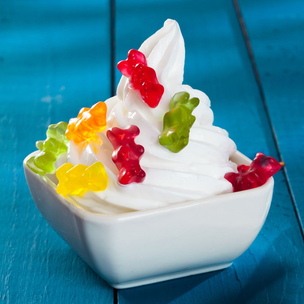 A Bowl Of Ice Cream With Gummi Bears As Topping On A Wooden Blue Background