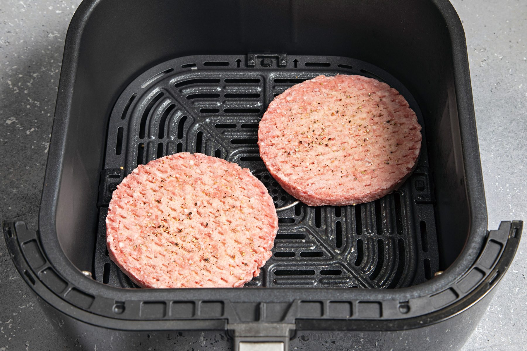 An air fryer basket with two raw beef patties