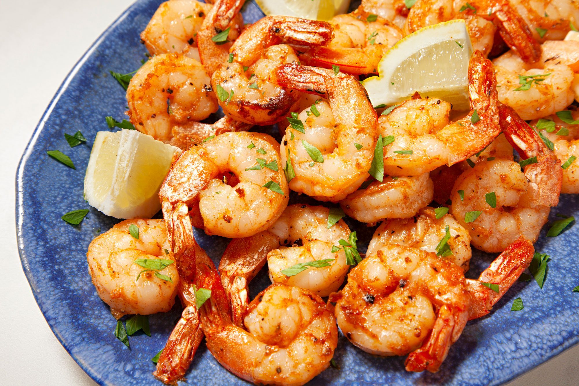 Air-Fryer Shrimp served on large blue textured platter with lemon wedges and sprinkle it with parsley over shrimp