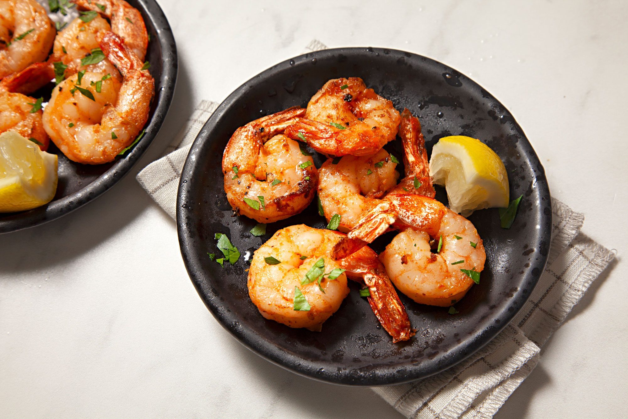 Air-Fryer Shrimp served on black small plates with lemon wedges, sprinkled with parsley