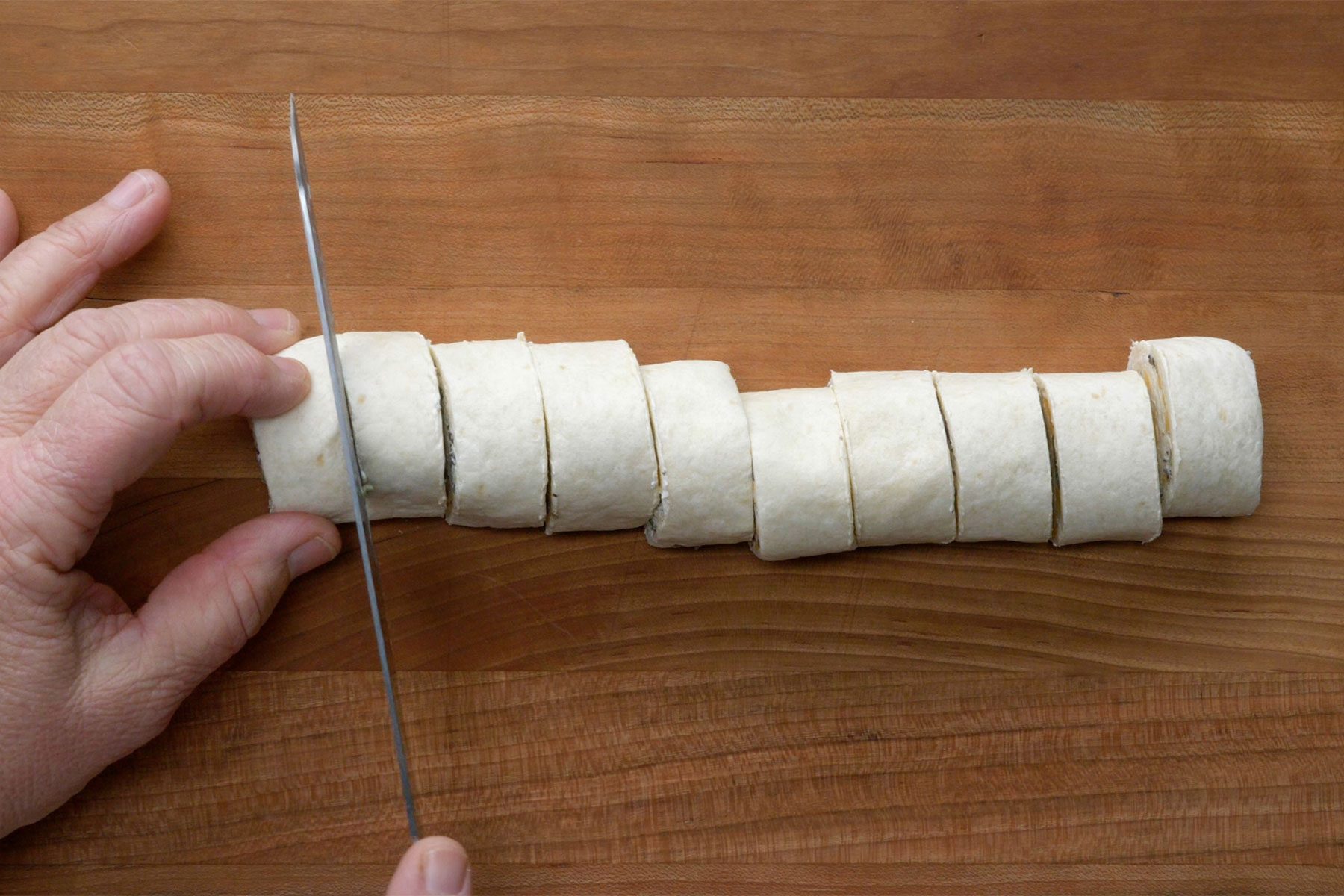 Overhead shot of unwrap roll; cut into slices; using a serrated knife; wooden background;