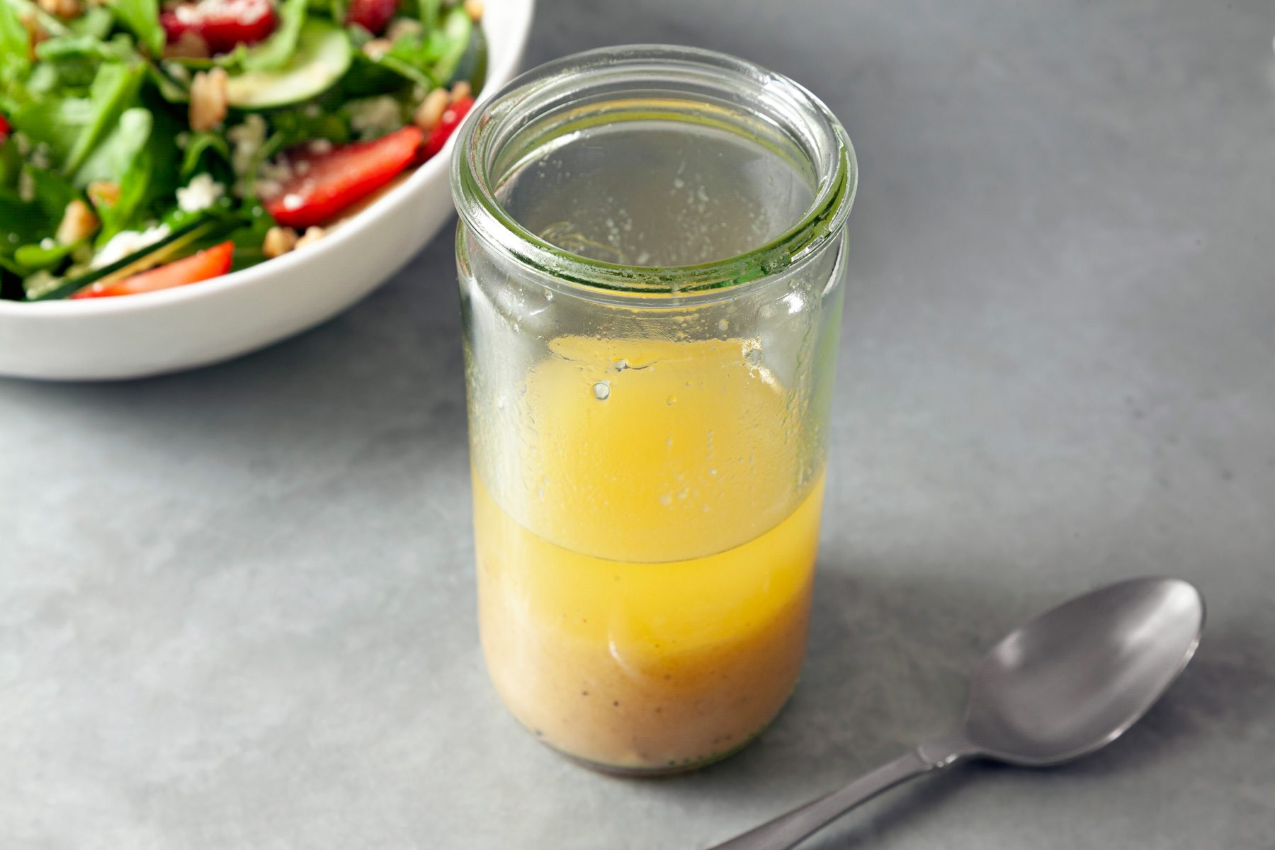 A jar of Apple Cider Vinaigrette with a bowl of salad