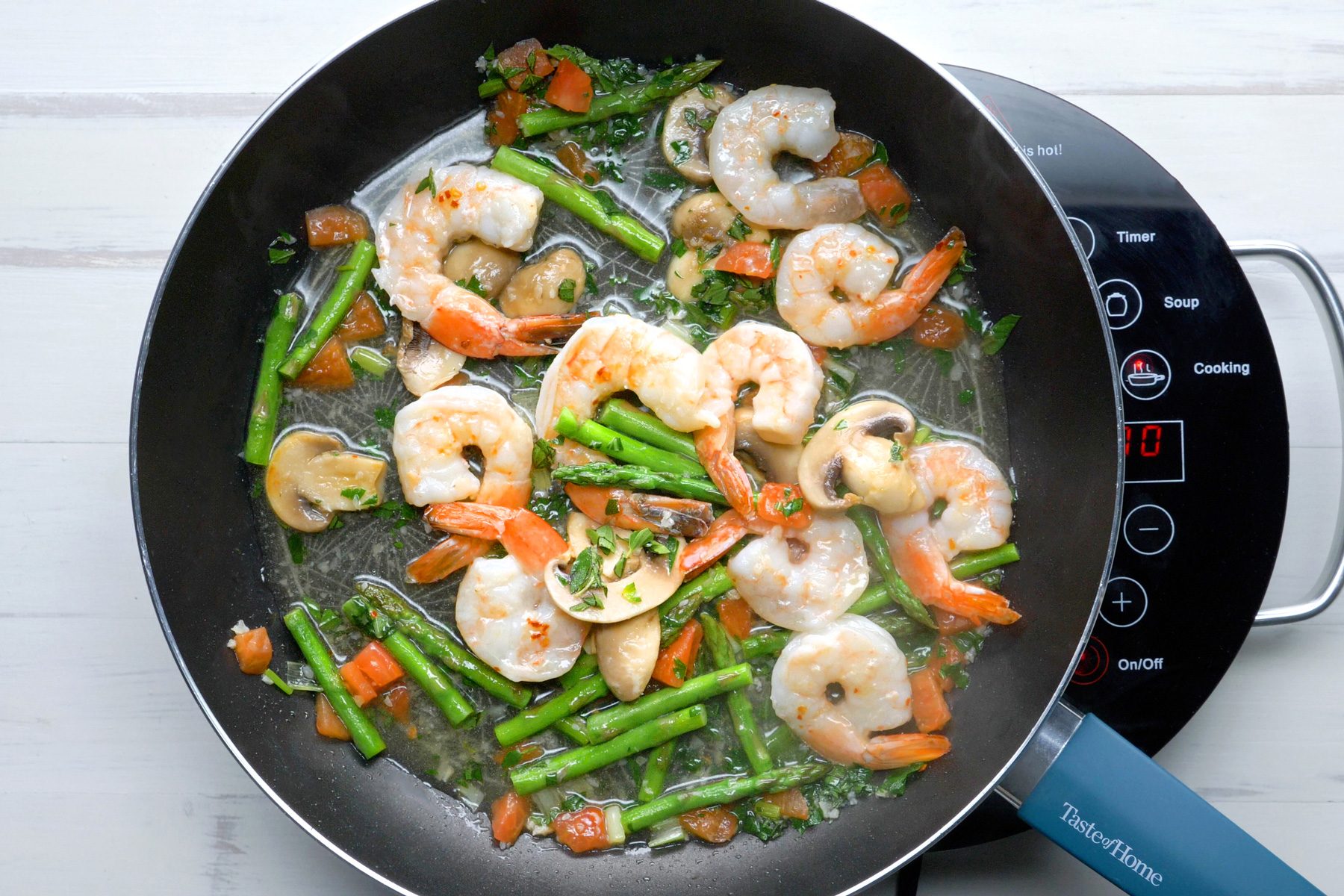 Asparagus, mushrooms, tomatoes, garlic, and onions cooking with shrimps in a small skillet