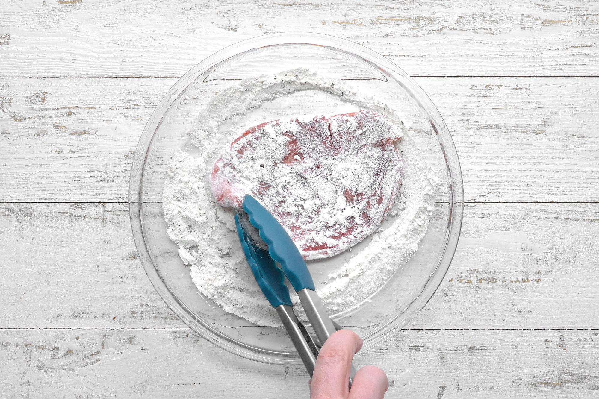 overhead shot; white wooden background; In a shallow dish; combine flour, salt and pepper; Add cutlets; turn to coat; with tong;