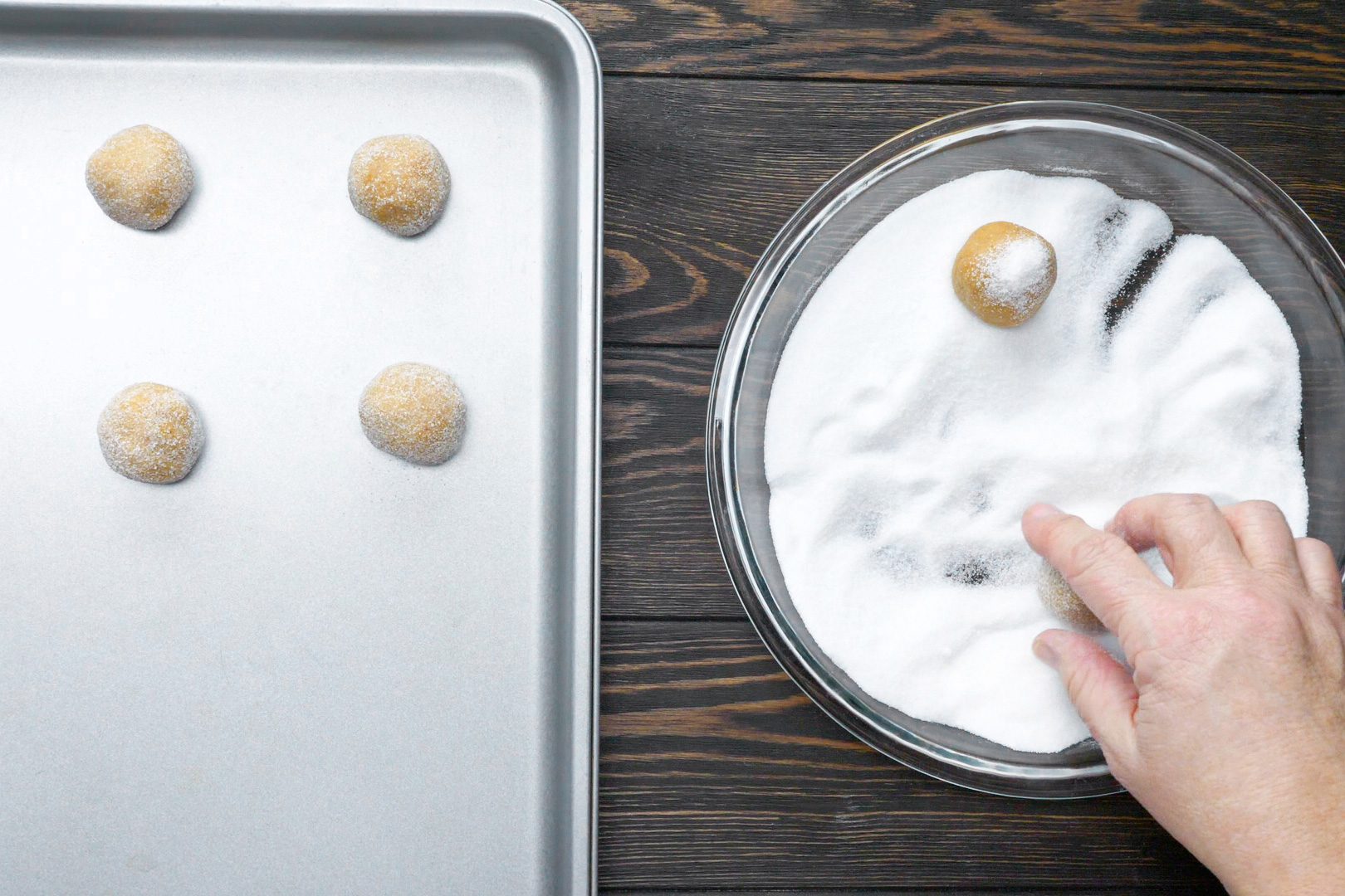 A person rolling the dough and placing prepared balls on a baking sheet