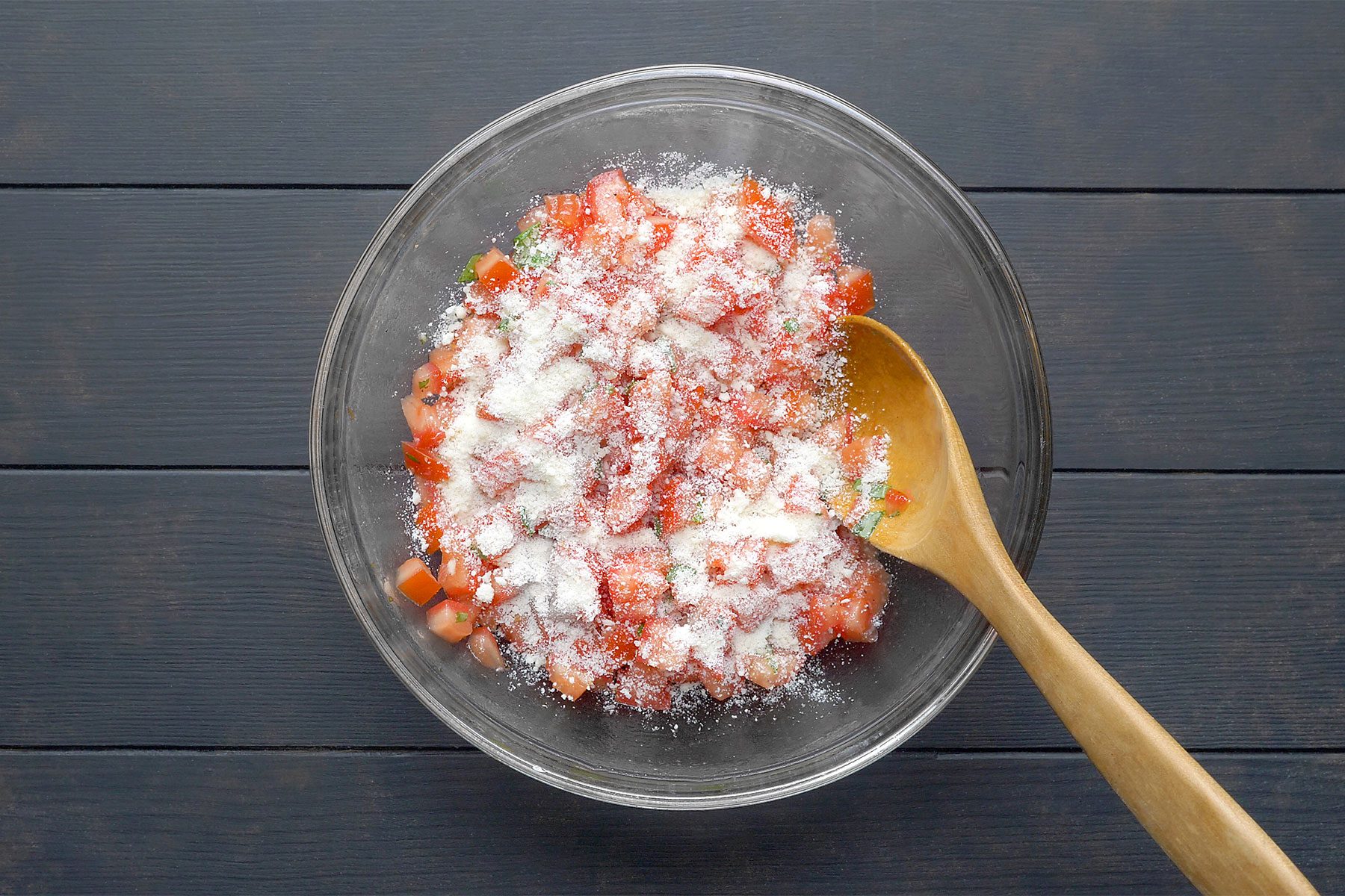 overhead shot; dark wooden background; In a large bowl, combine oil, basil, garlic, salt and pepper; wooden spatula;