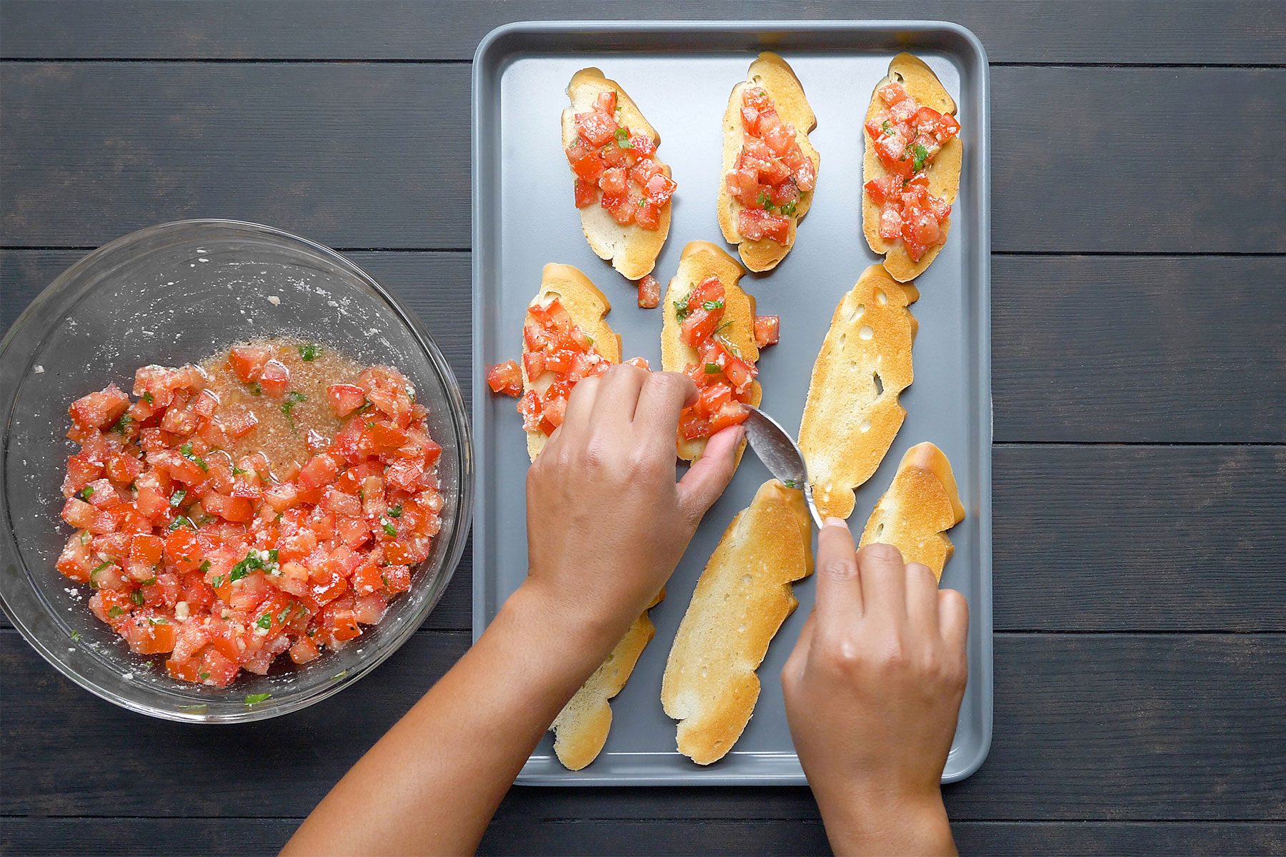 overhead shot; dark wooden background; bread toast pieces; Topped with tomato mixture; on large rectangular tray;