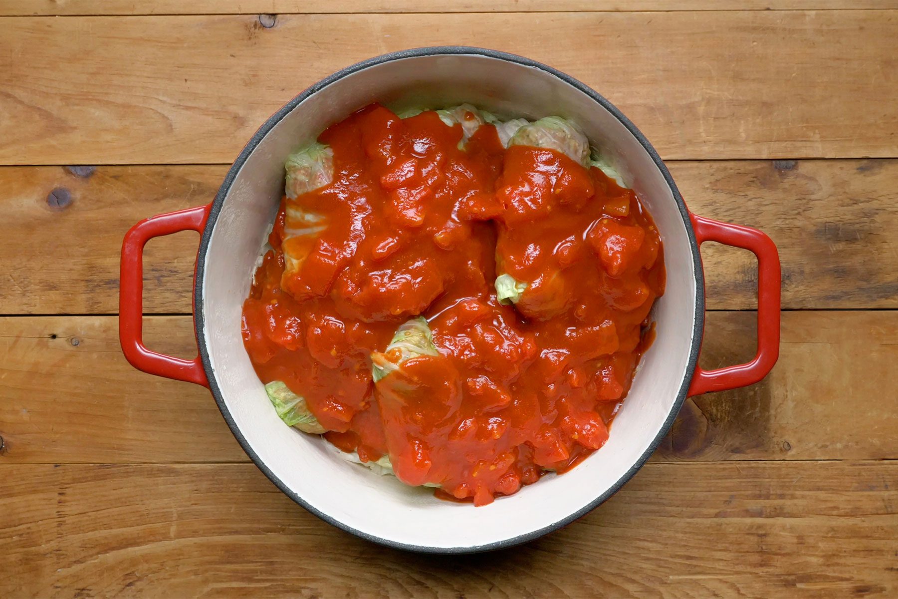 overhead shot of tomato sauce poured over cabbage rolls in a dutch oven