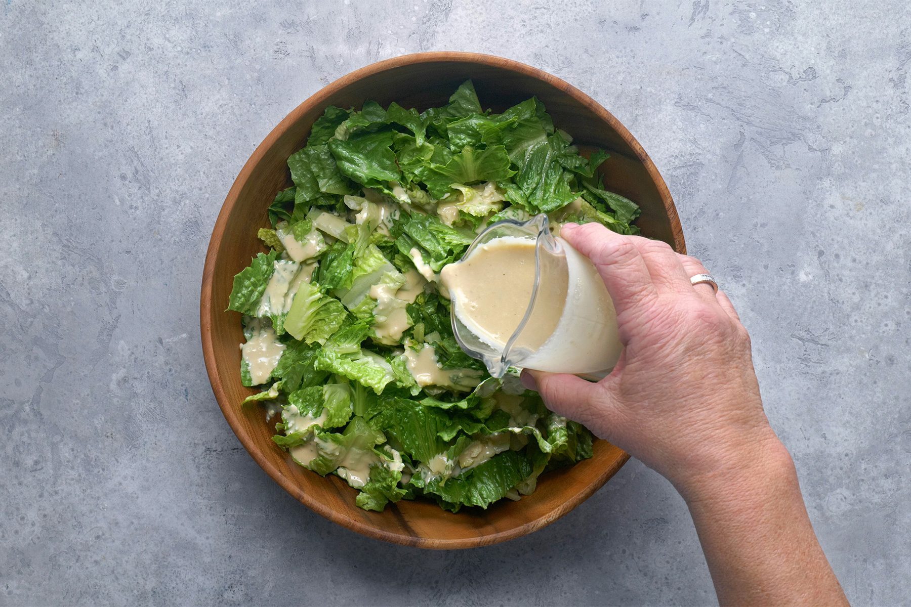 Overhead shot of place romiane into large salad bowl; drizzle with dressing; grey background