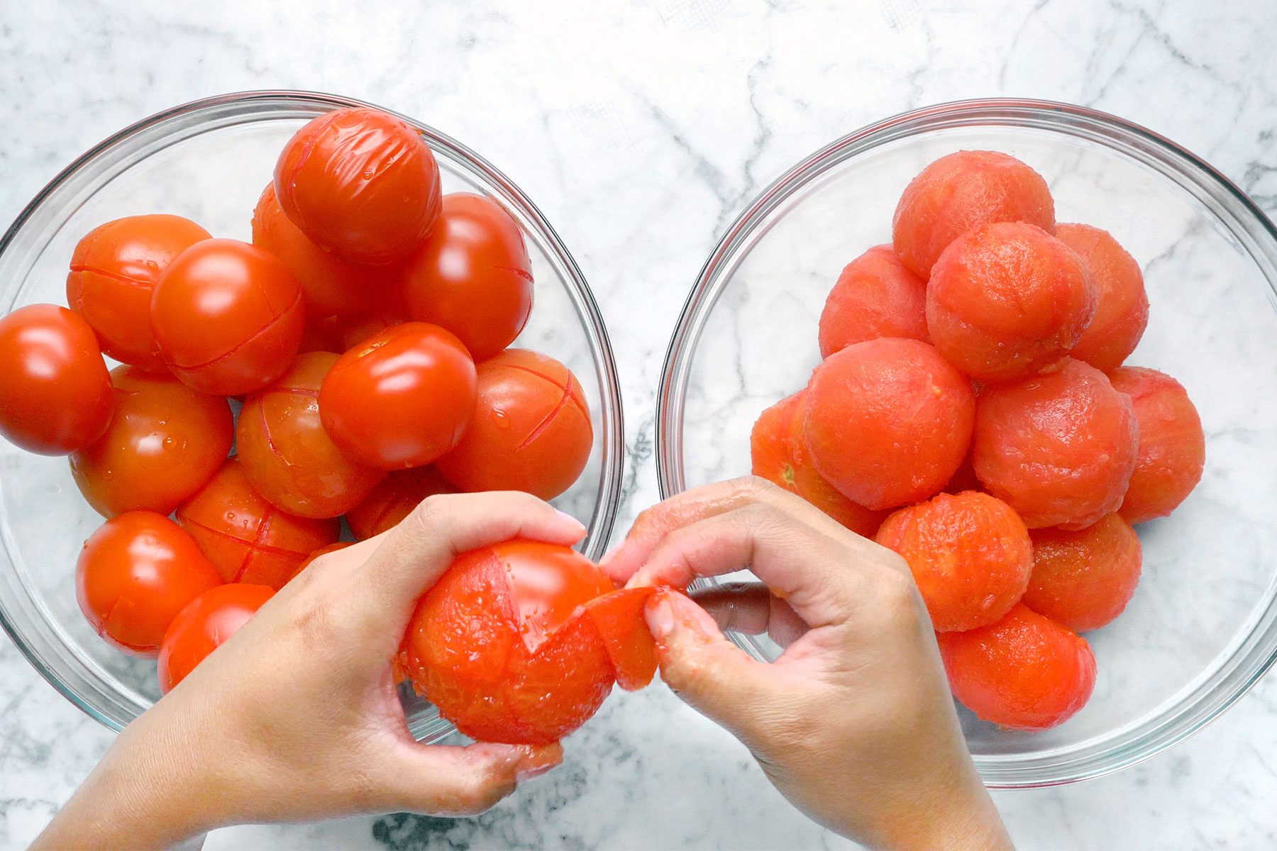 Overhead shot of peeling tomatos; two glass bowls; marble background;