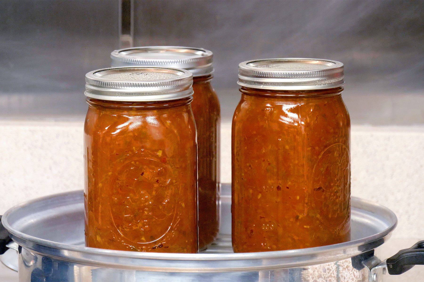 Table view shot of placed jars into canner with simmering water; bring to a boil; process for 40 minutes; remove jars and cool;