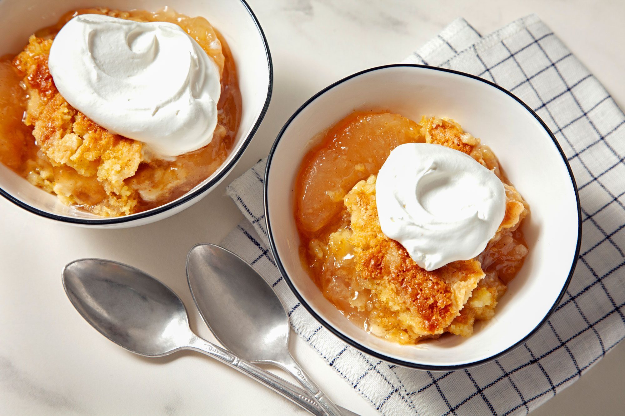 high angle shot of caramel apple dump cake served in two bowls topped with whipped cream; marble background;