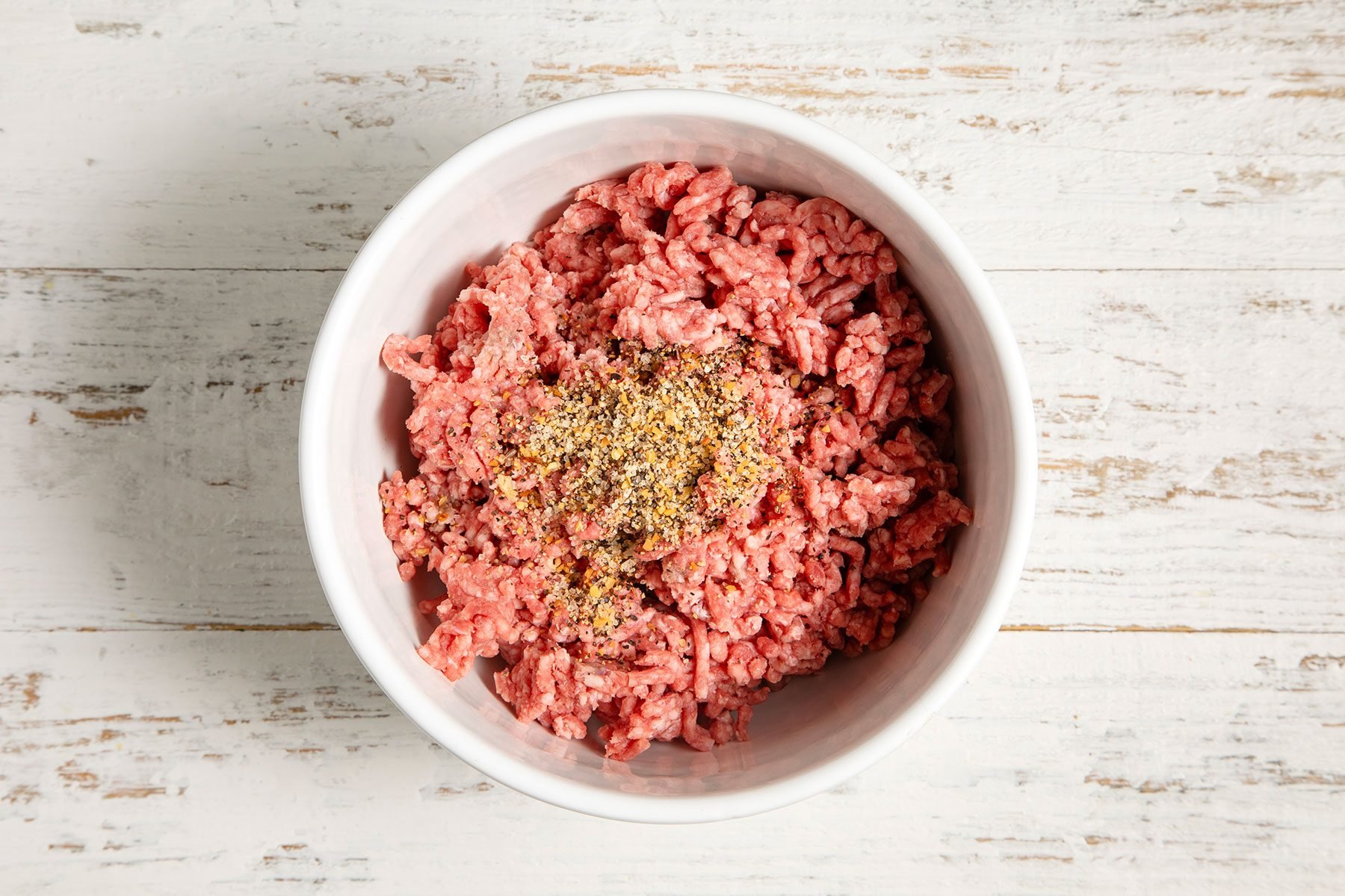 overhead shot; white textured background; In a large bowl, combined beef and steak seasoning;