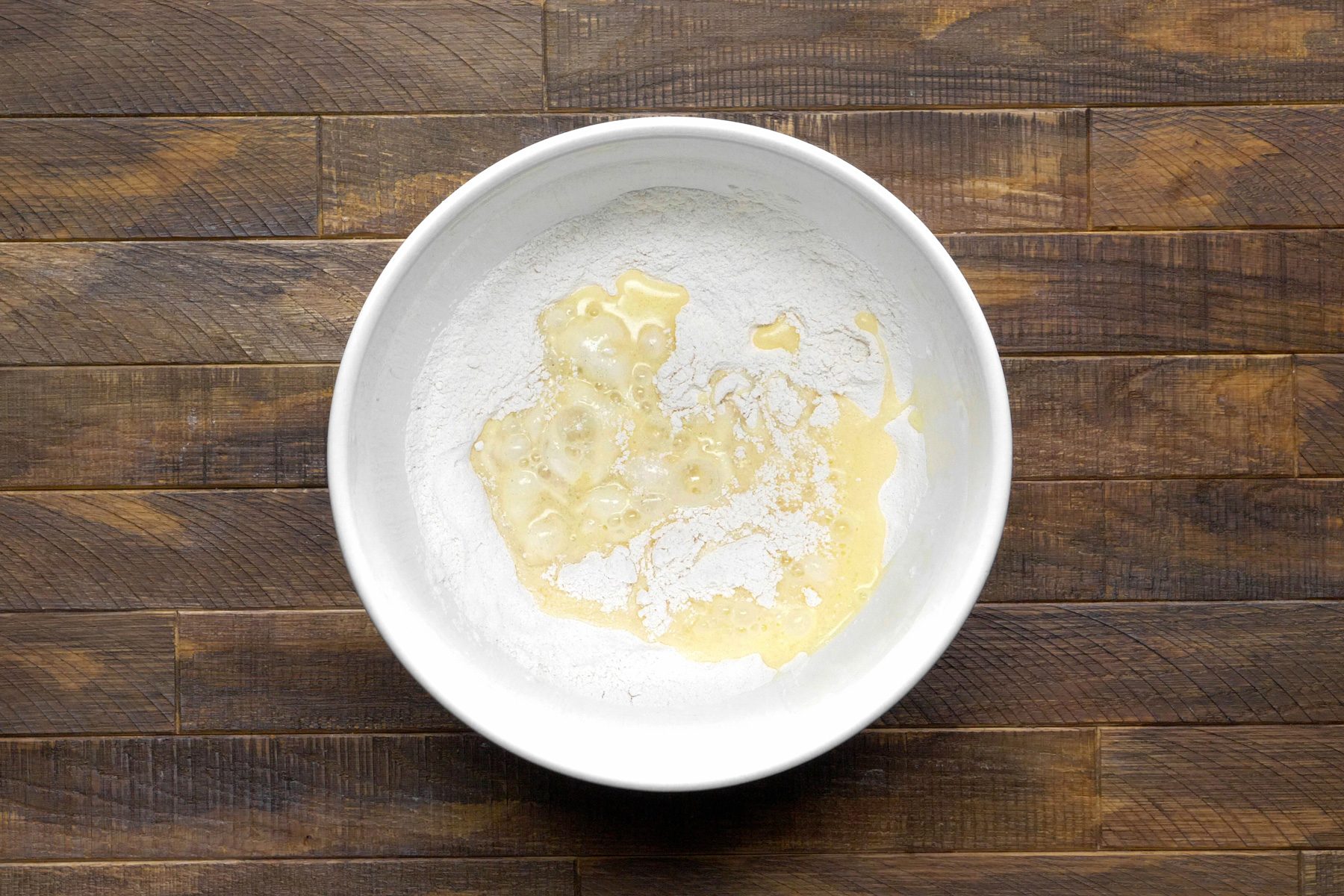 A white bowl of a mixture of egg, milk, oil and flour.
