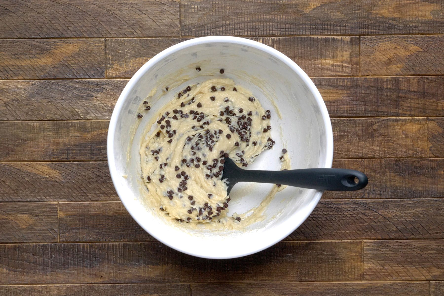 A white bowl of a batter with chocolate chips.