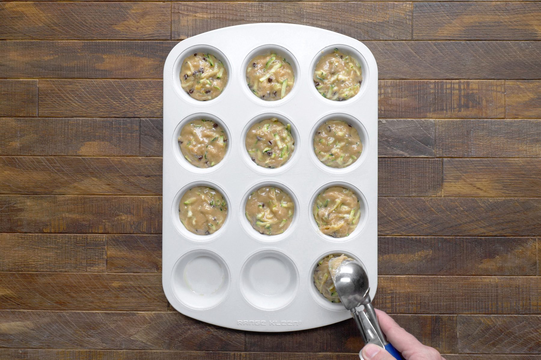 A hand filling a muffin cup tray with batter