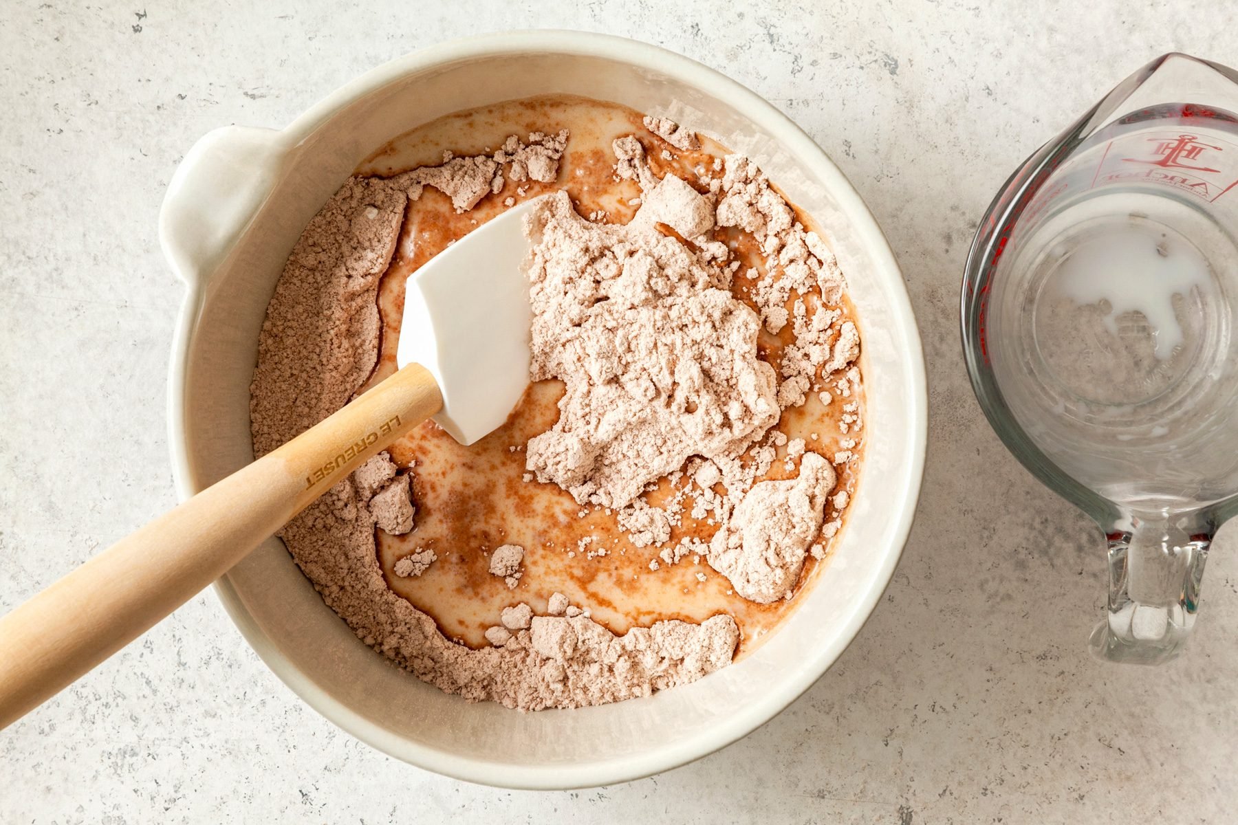 A bowl of batter with a wooden spoon and a measuring cup