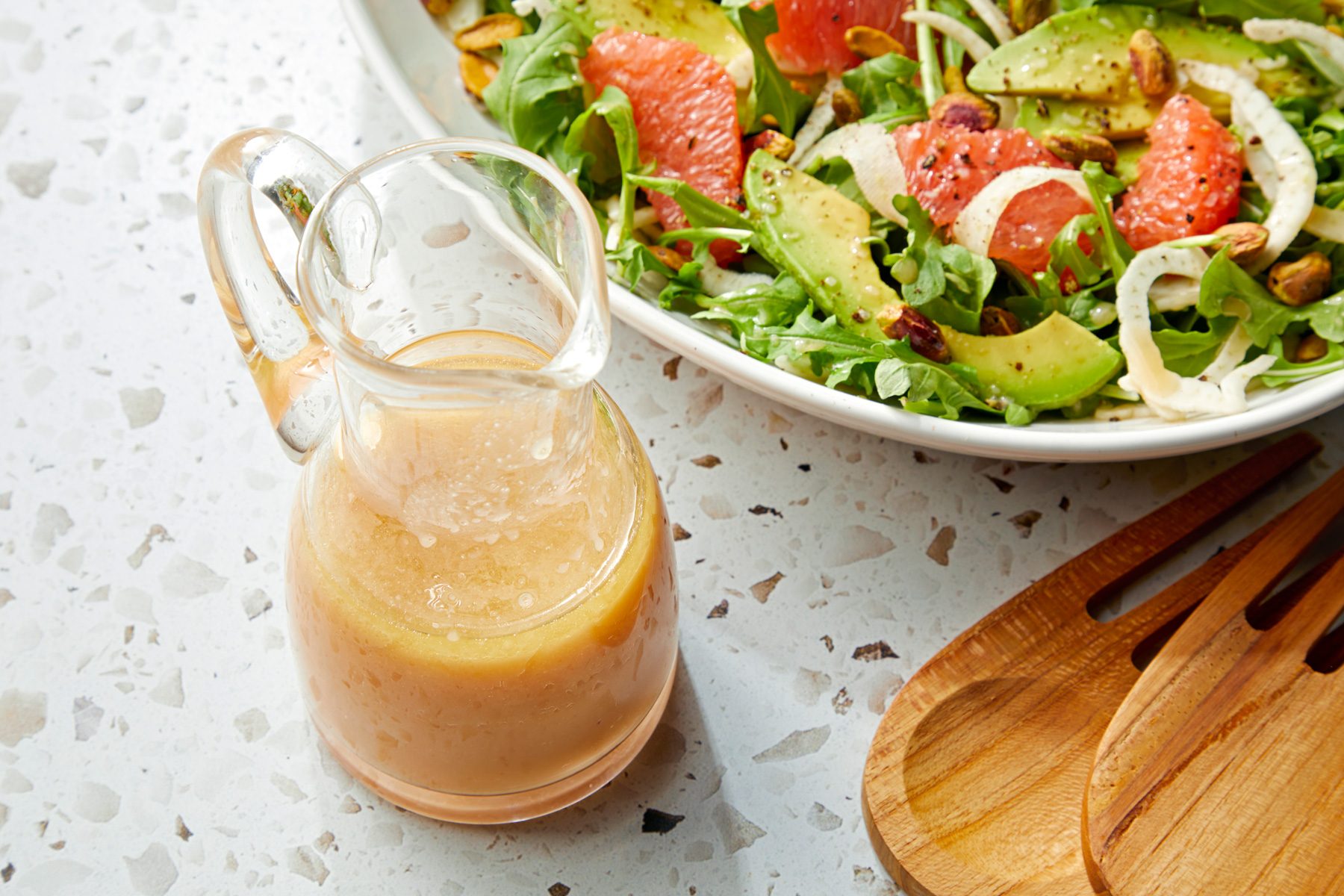 A glass pitcher of Citrus Vinaigrette dressing is next to a bowl of mixed salad
