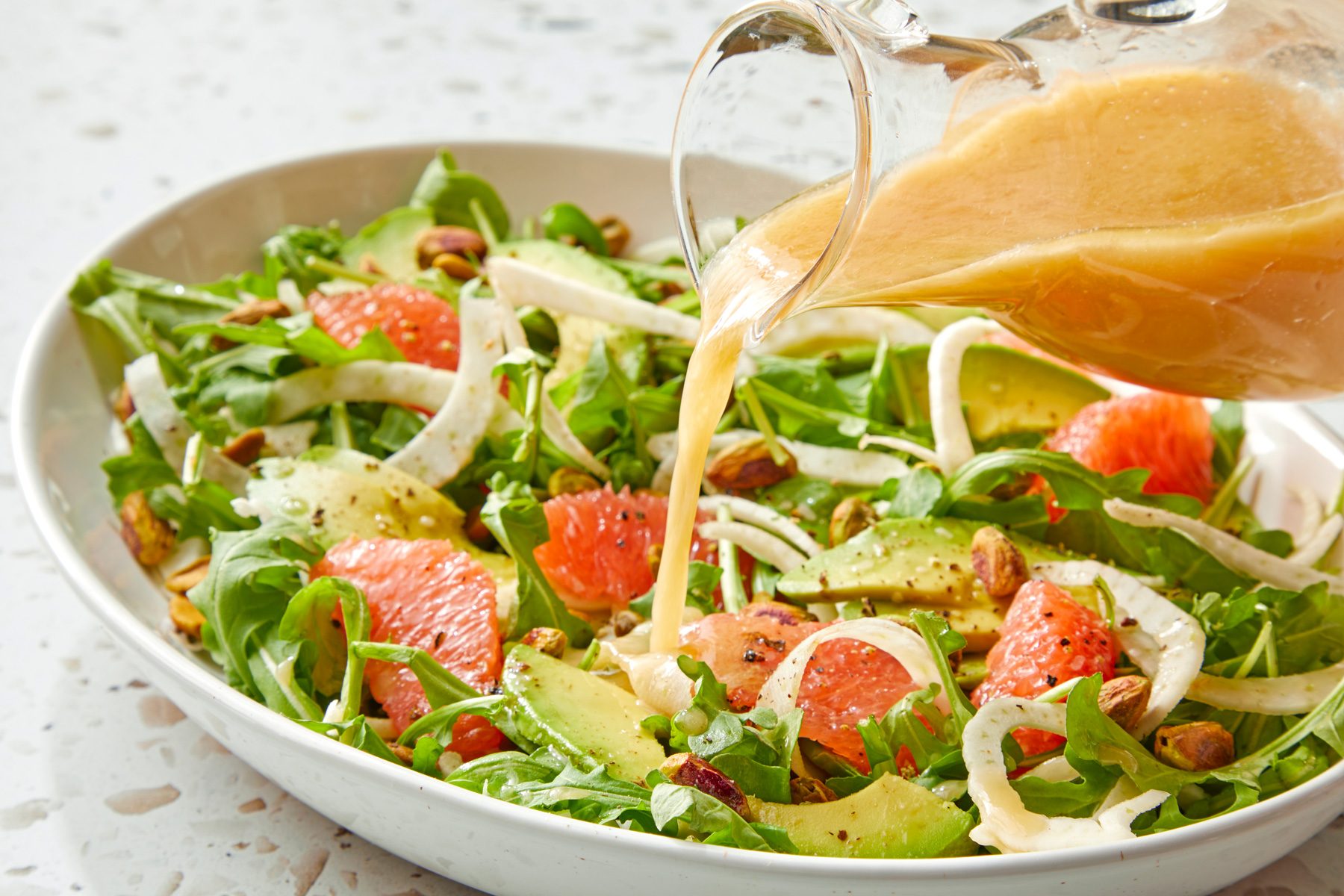 Citrus vinaigrette being poured over a bowl of salad