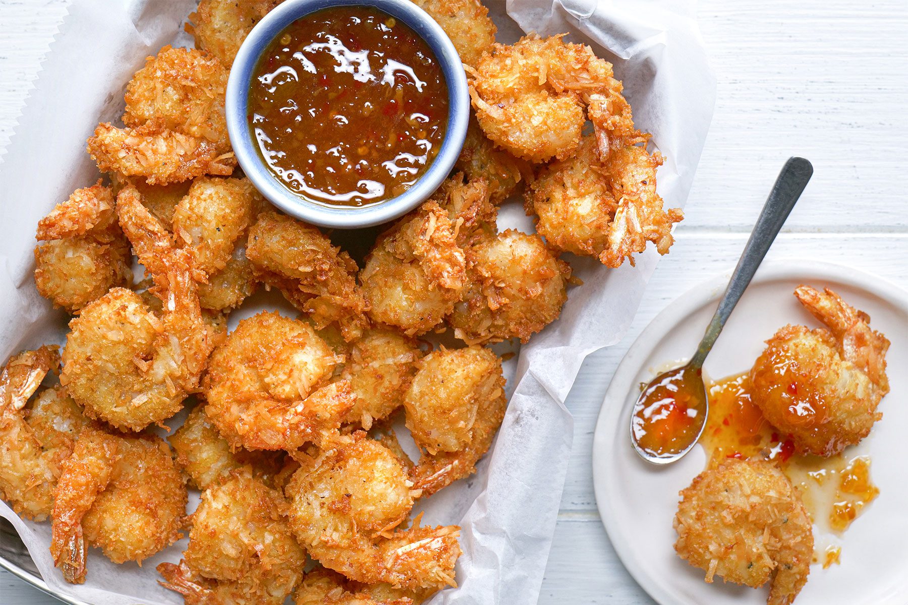 Overhead shot of Tasty Coconut Shrimp; served on small white plate with sauce; white wooden background;