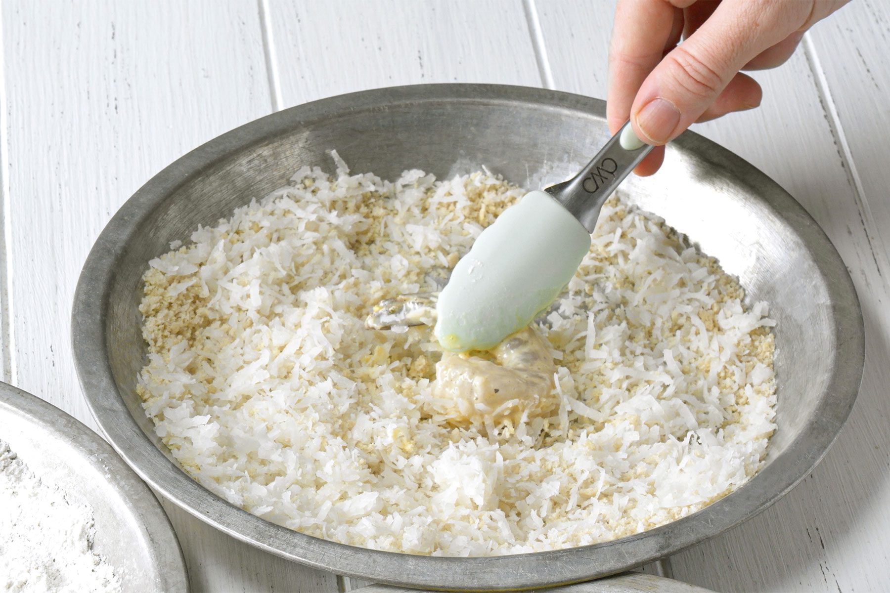 3/4 angle view shot of third prepared bowl; dip in bread crumb mixture; tongs; white wooden background;