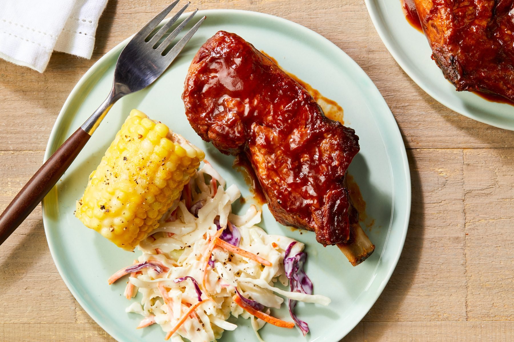 A plate of country Ribs in The Oven served with corn on the cob and a salad