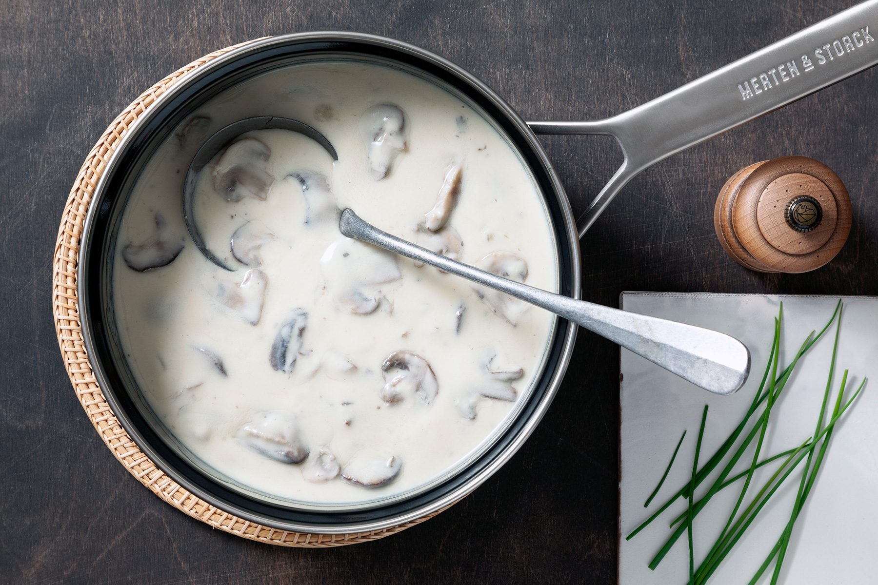 Overhead shot of Quick Cream of Mushroom; in large saucepan; table mat; white tray; serving spoon; dark texture background;