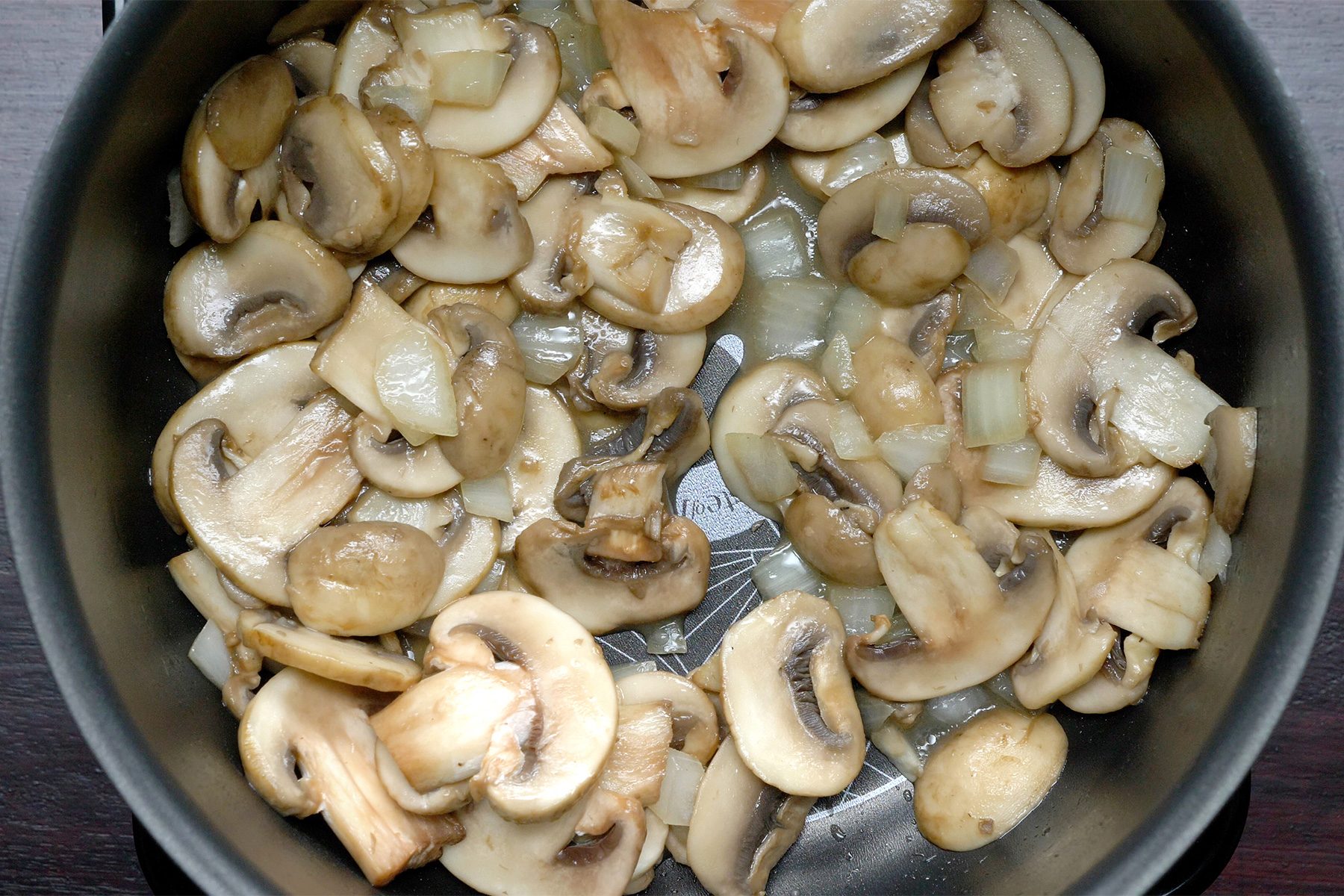 Close shot of a large saucepan; heat butter over medium-high heat; saute mushrooms and onion until tender; dark wooden background;