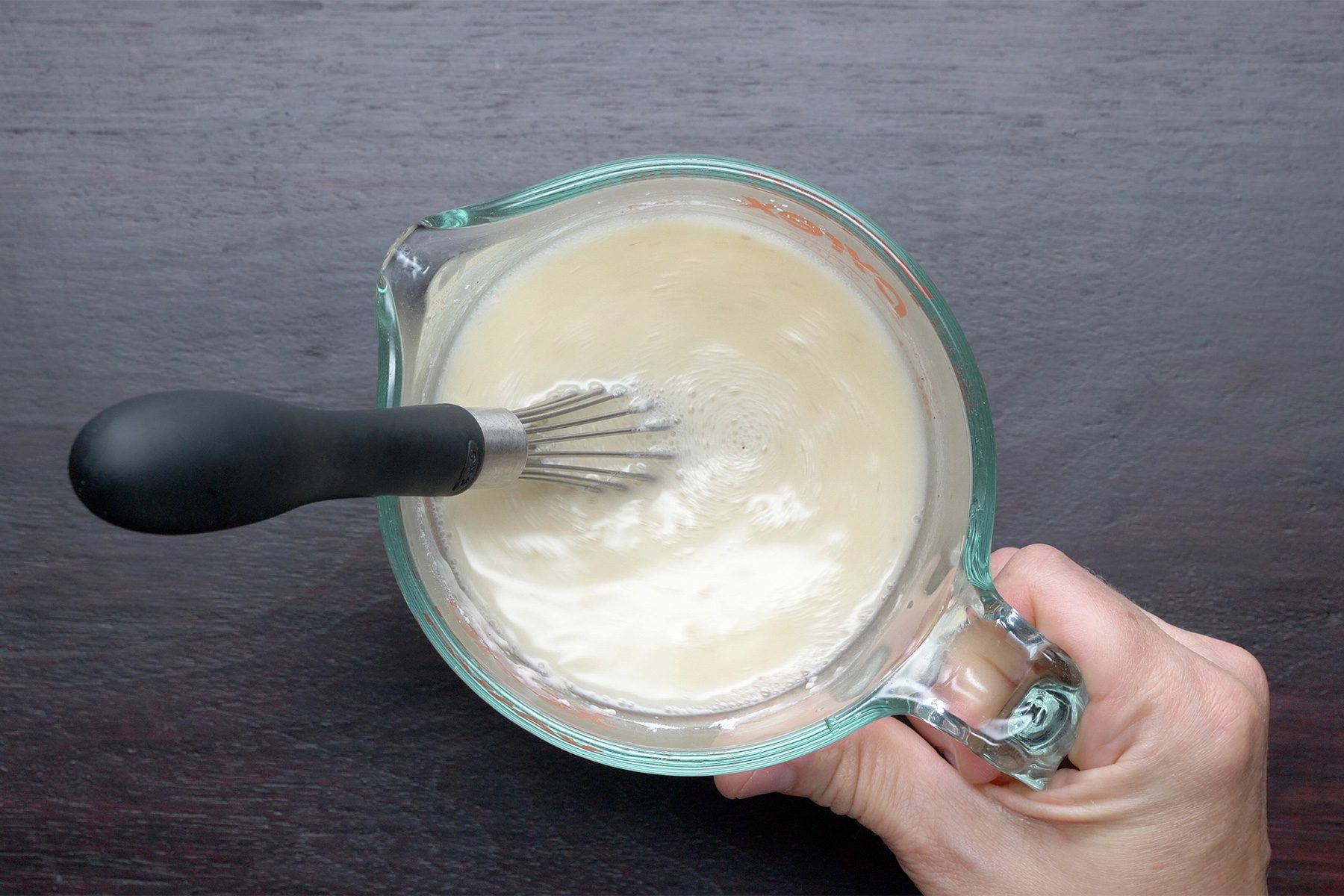 Overhead shot of mix flour; salt; pepper and 1 can broth until smooth; whisk tool; dark wooden background;