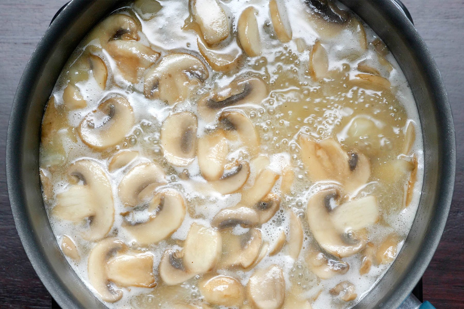 Close shot of adding mixture into mushroom; stir in remaining can of broth; bring to a boil; saucepan; dark wooden background;