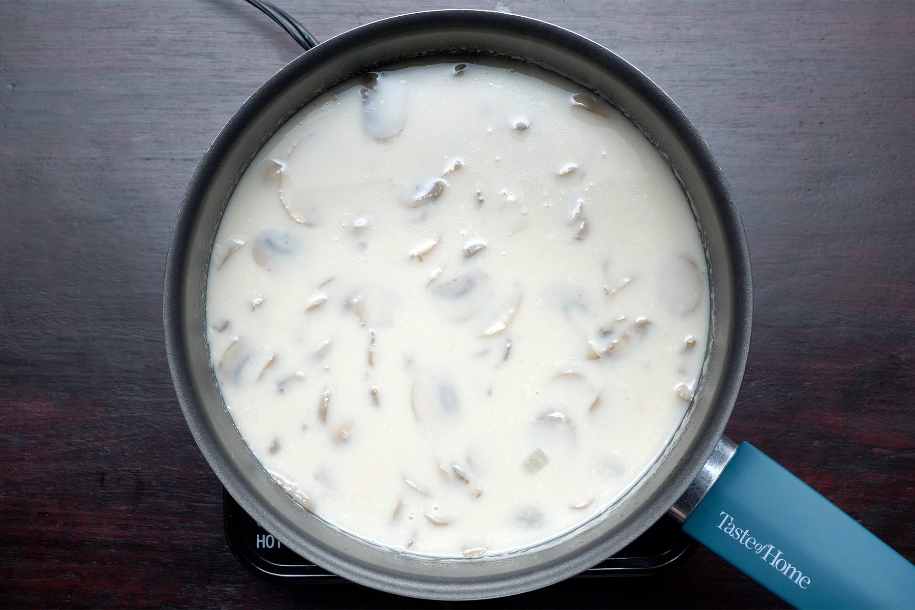 Overhead shot of same saucepan; reduce heat; stir in cream; simmer; uncovered until flavors are blended; stirring occasionally; dark wooden background;