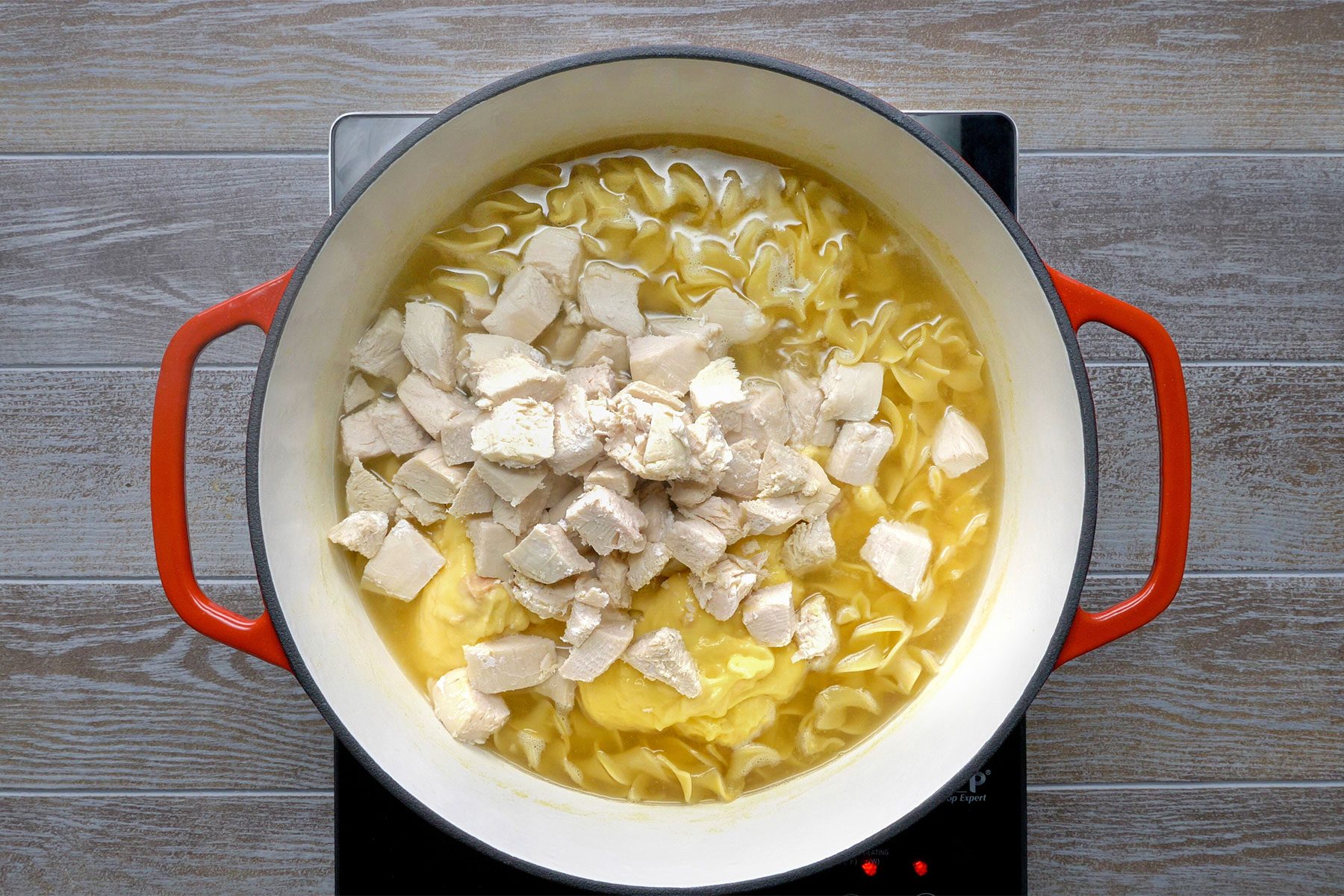 Overhead shot of add soup and chicken; induction; light brown wooden background;