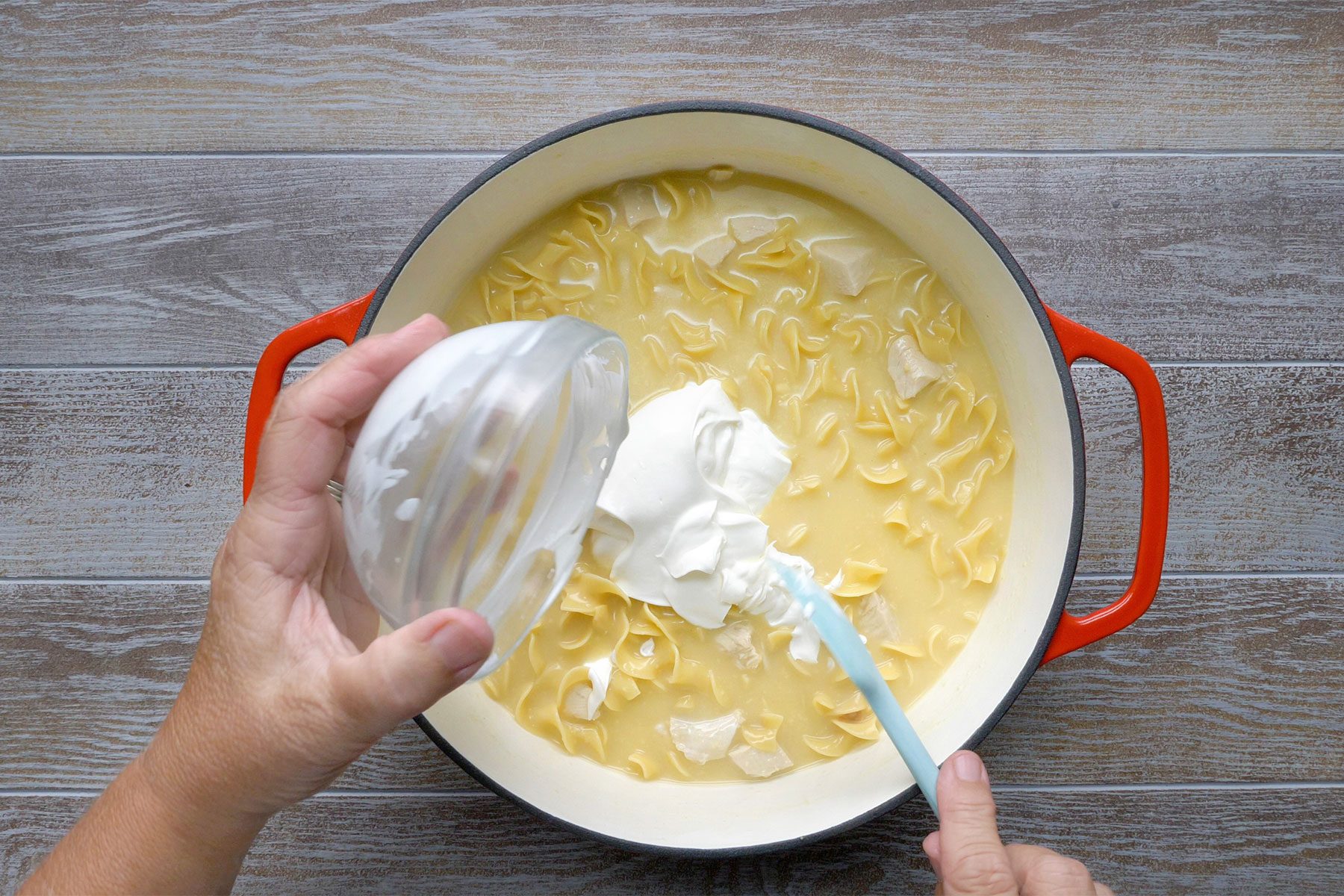 Overheda shot of a same saucepan; remove from heat; stir in the sour cream; spatula; light brown wooden background;