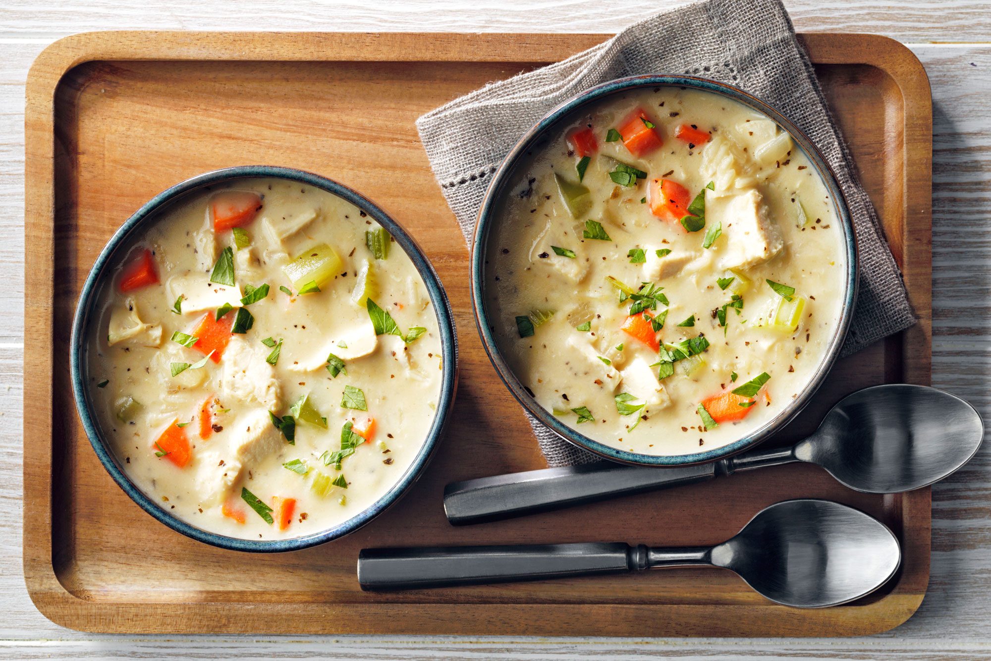 Two bowls of Creamy Chicken And Rice Soup on a wooden tray