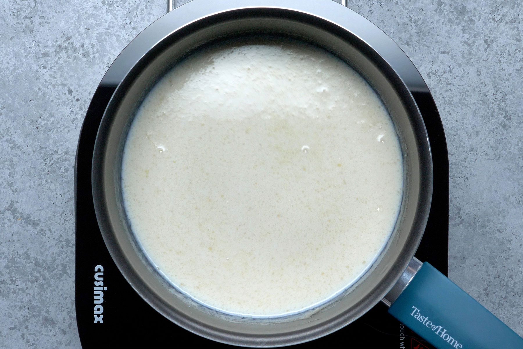 Overhead shot of a large saucepan; melt butter; stir in flour until smooth; gradually add1-1/2 cups milk; bring to a boil; cook and stir until thickened; induction; grey marble texture background;