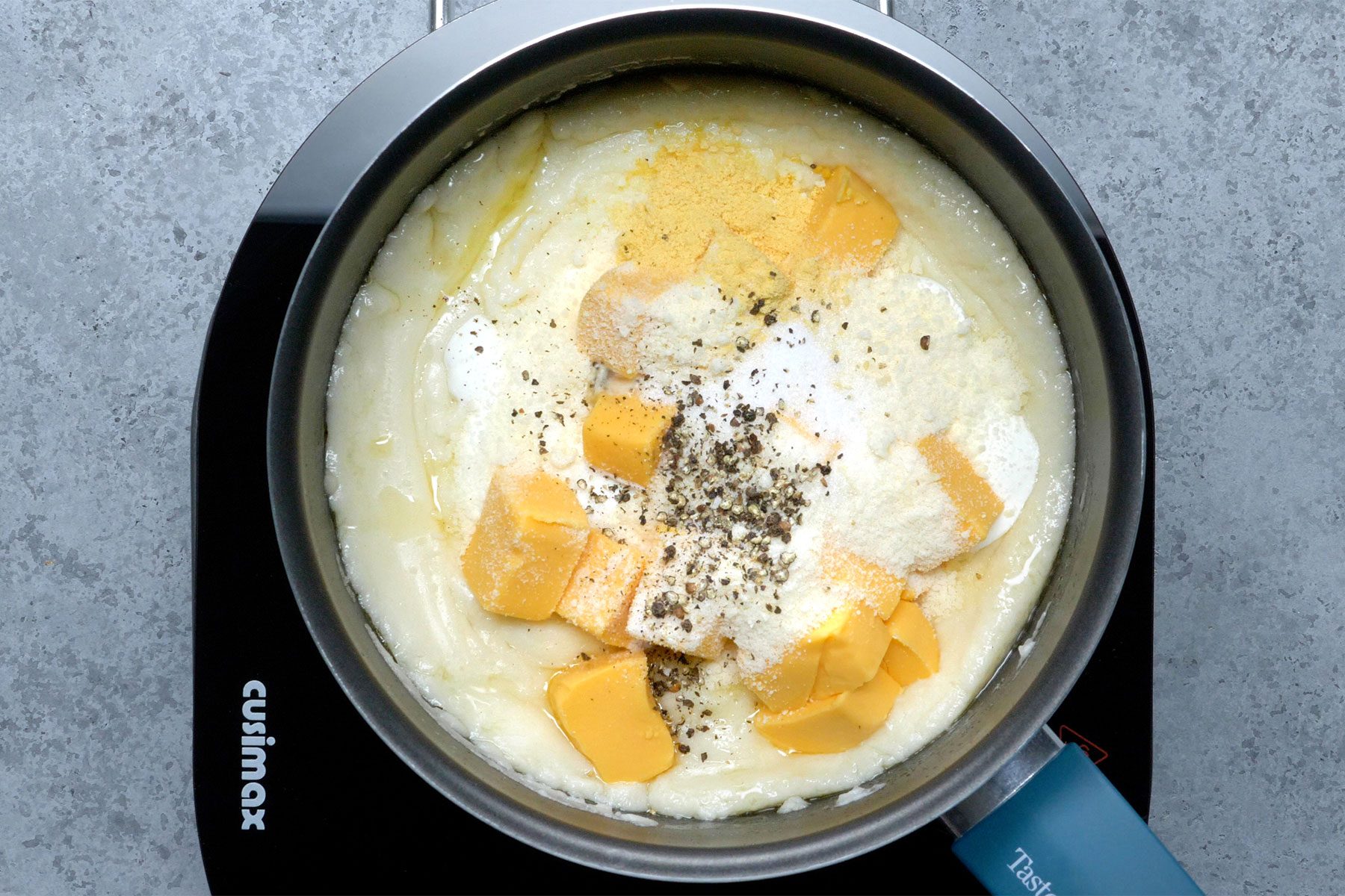 Overhead shot of a same saucepan; stir in sour cream; velveeta; parmesan cheese; salt; mustard and pepper until smooth and cheese is melted; induction; grey marble texture background;