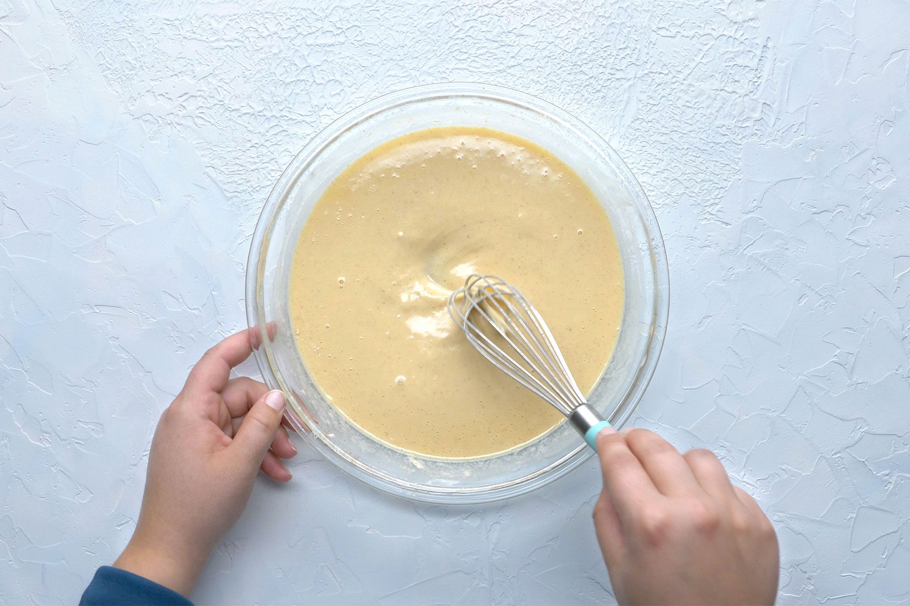 overhead shot; white textured background; in a large bowl onion rings batter; whisker;